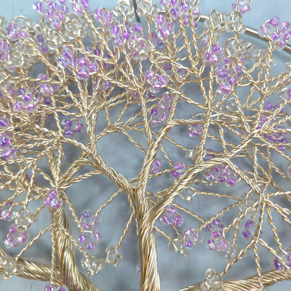 Decorative wall art with gold tree branches and purple beads on a light blue background
