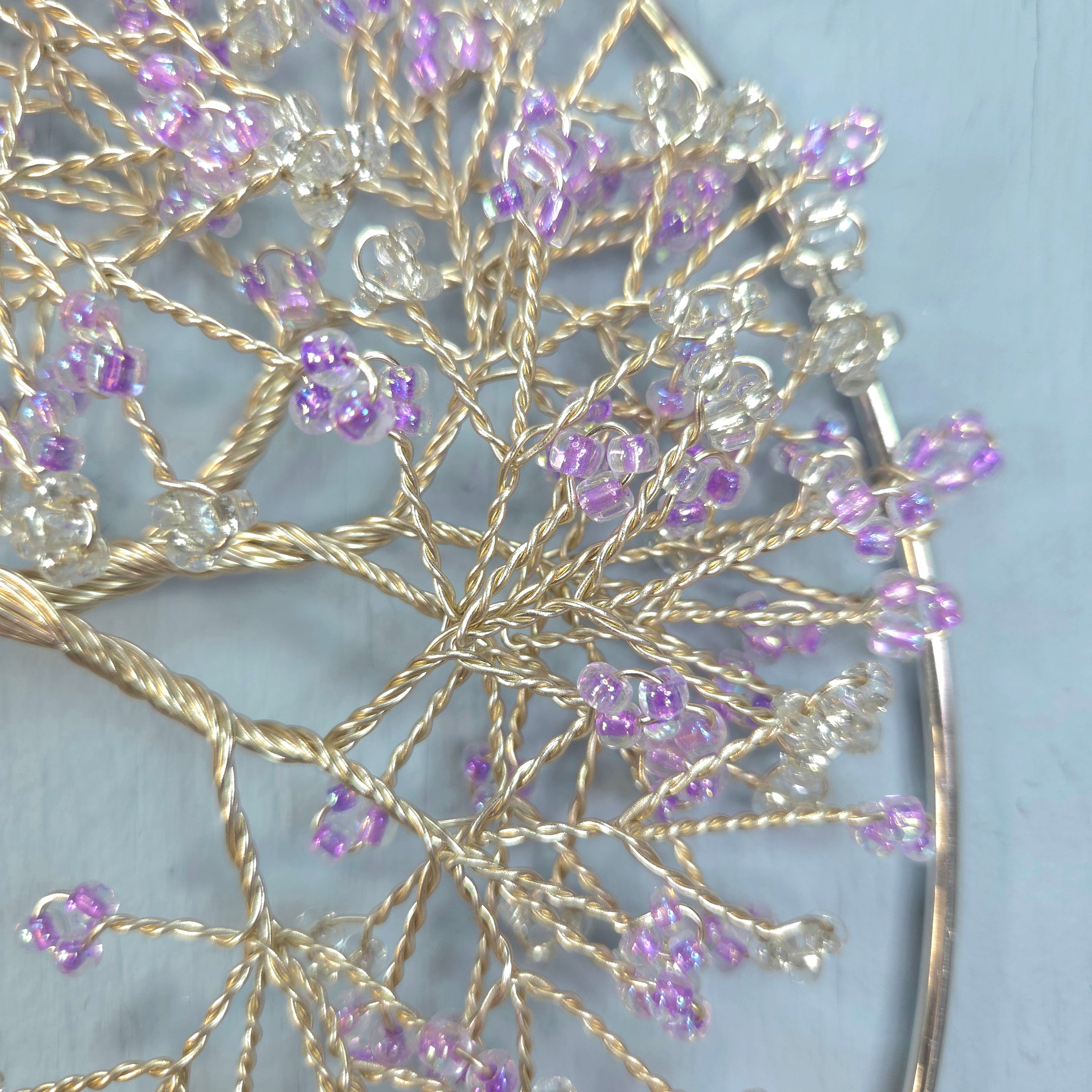 Decorative hairpin with gold wire and purple beads on a light blue background