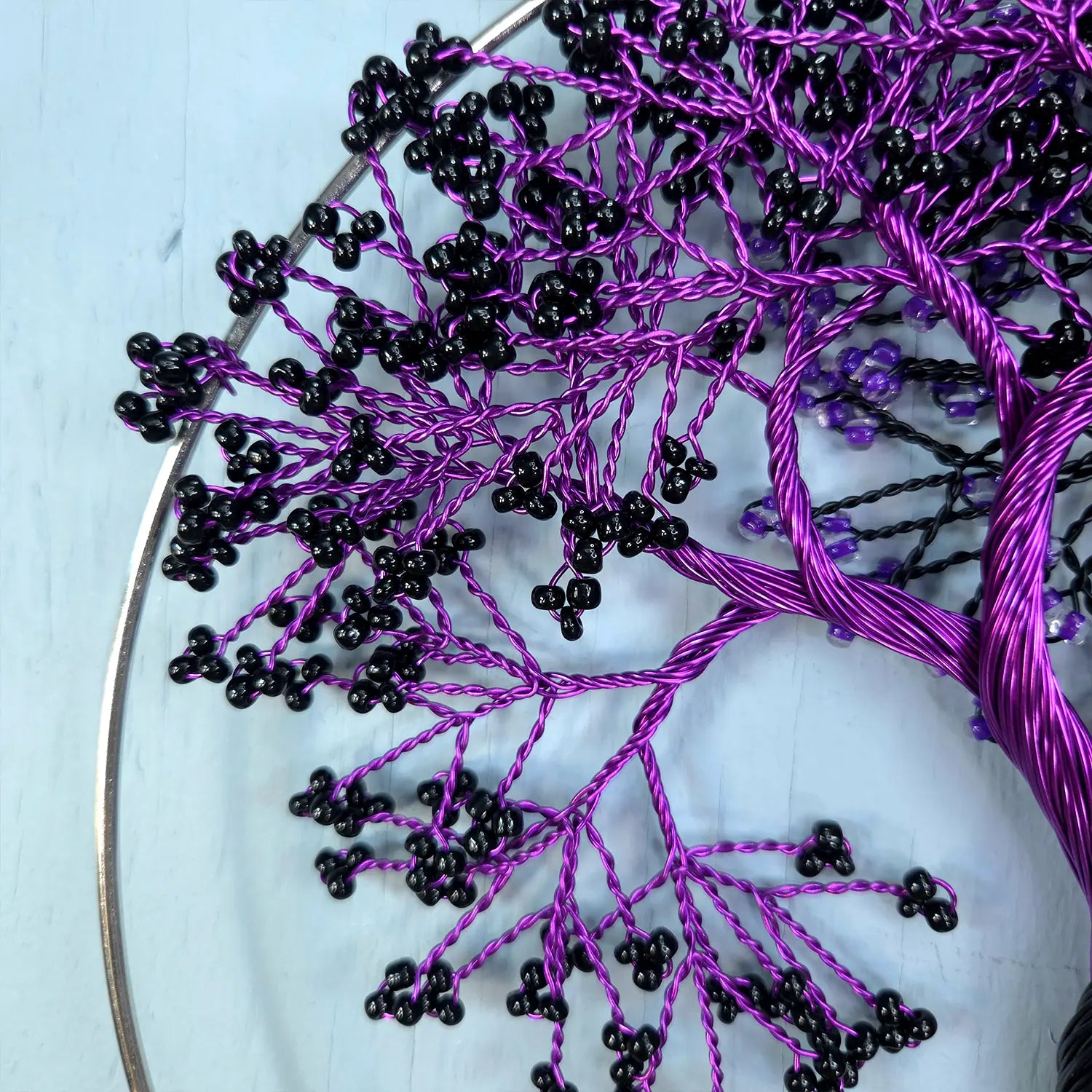 Embroidery hoop with black and purple thread creating a tree-like pattern on a light blue background.