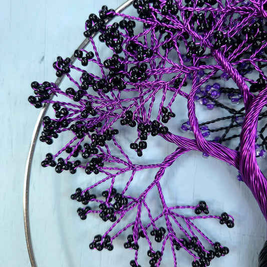Embroidery hoop with black and purple thread creating a tree-like pattern on a light blue background.