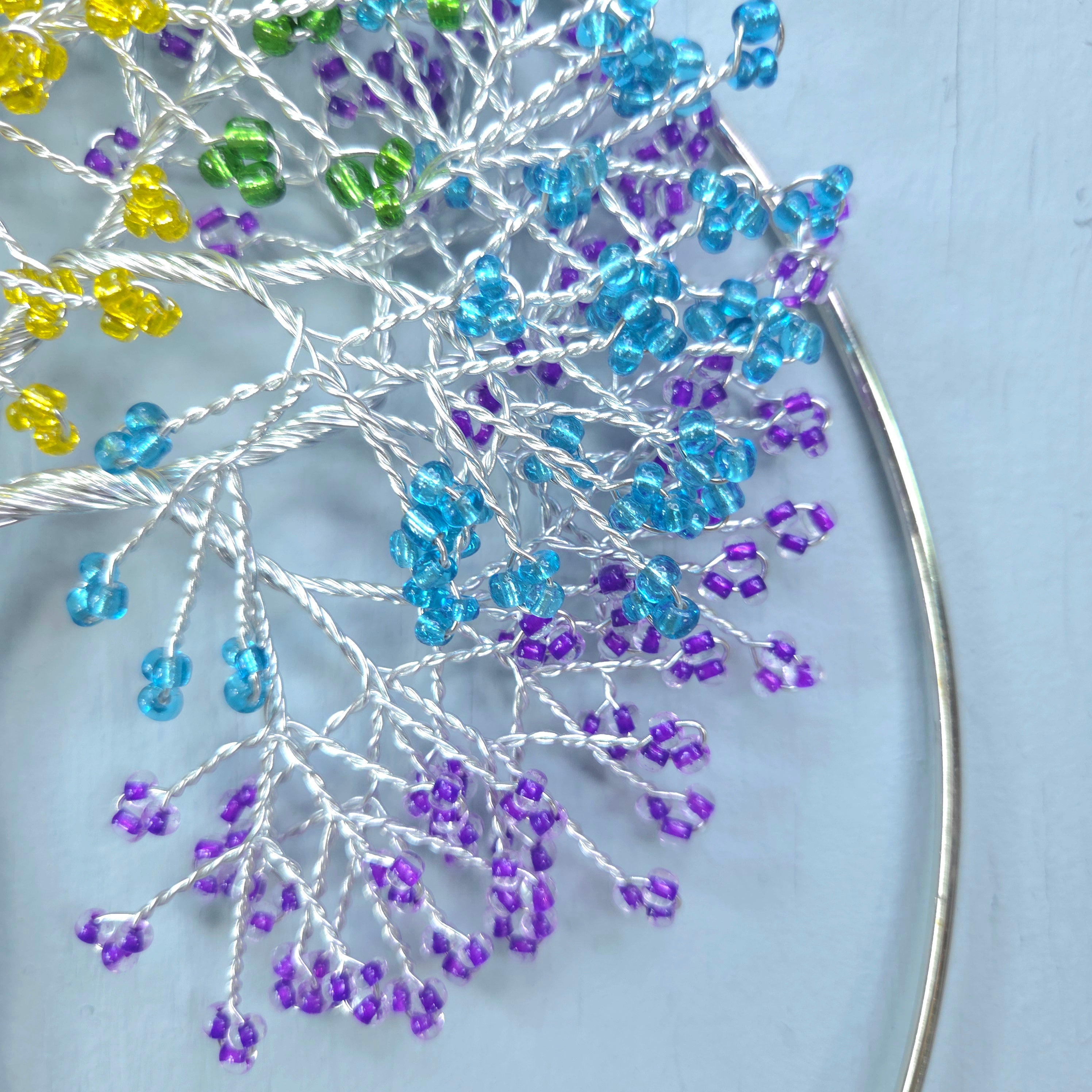 Close-up of a beaded flower with blue, purple, and yellow beads on a light blue background.