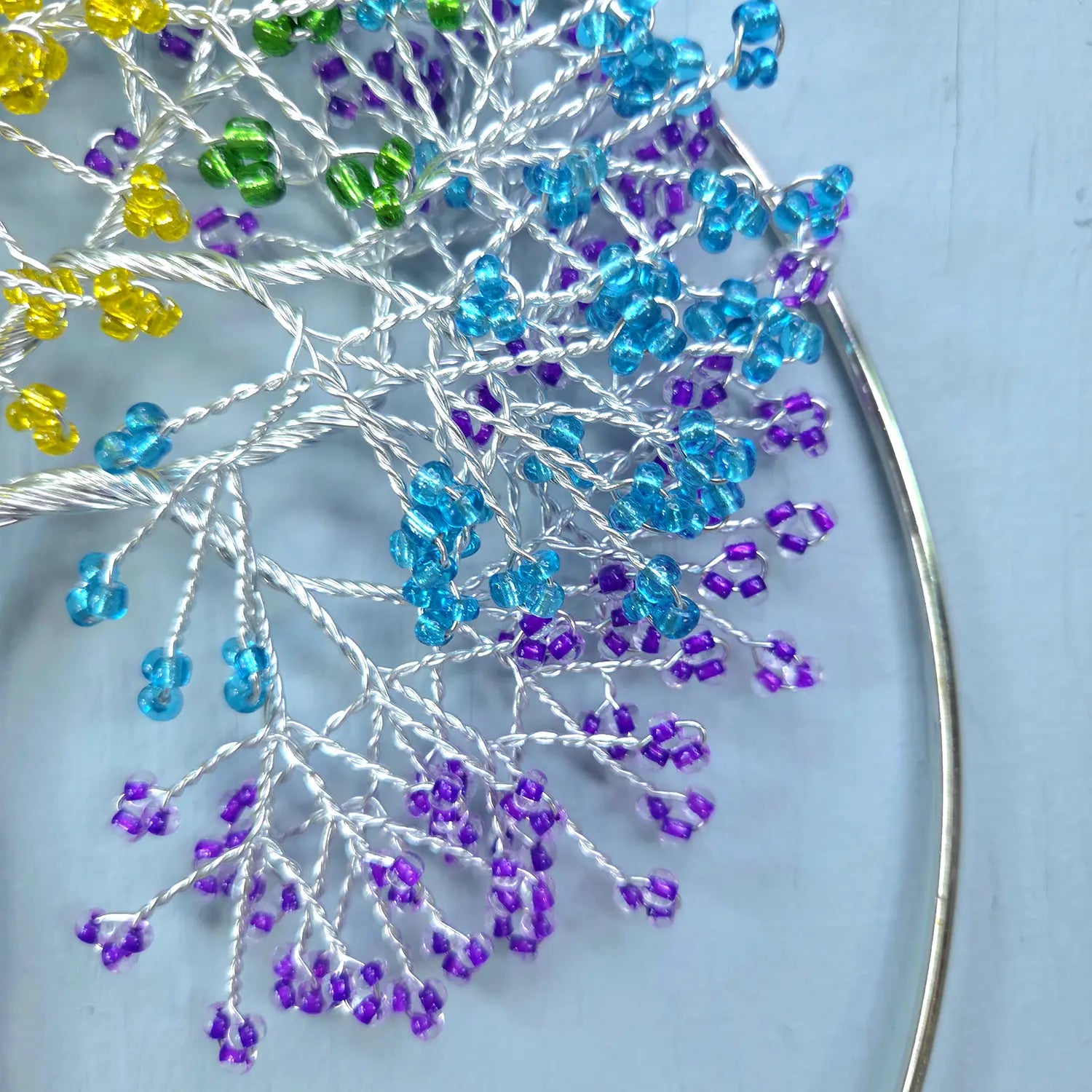 Close-up of a beaded flower with blue, purple, and yellow beads on a light blue background.