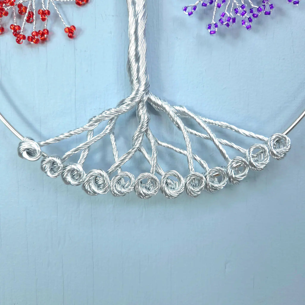 Silver wire tree of life necklace on a light blue background with red and purple beads.