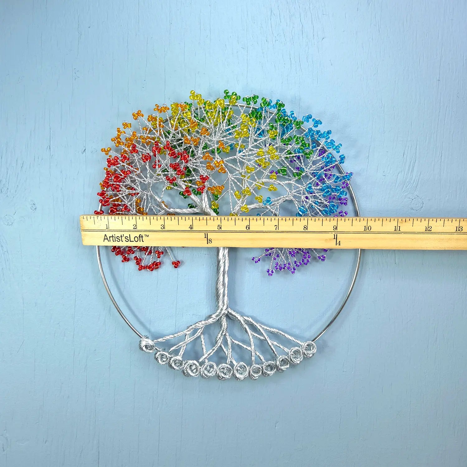 Colorful tree-shaped wall art with a ruler for scale on a light blue background