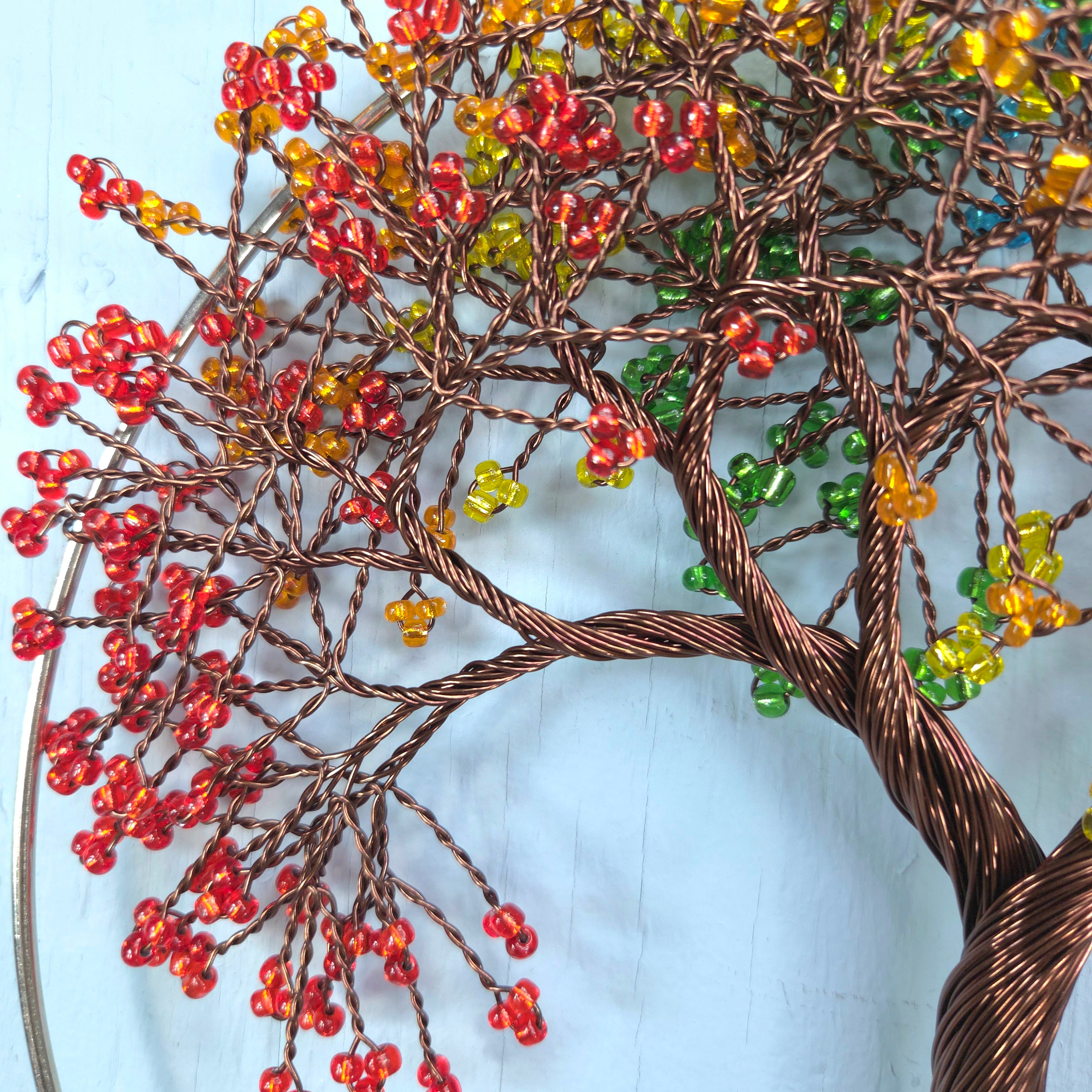 Decorative wall art of a tree with red, orange, and green beads on a light blue background