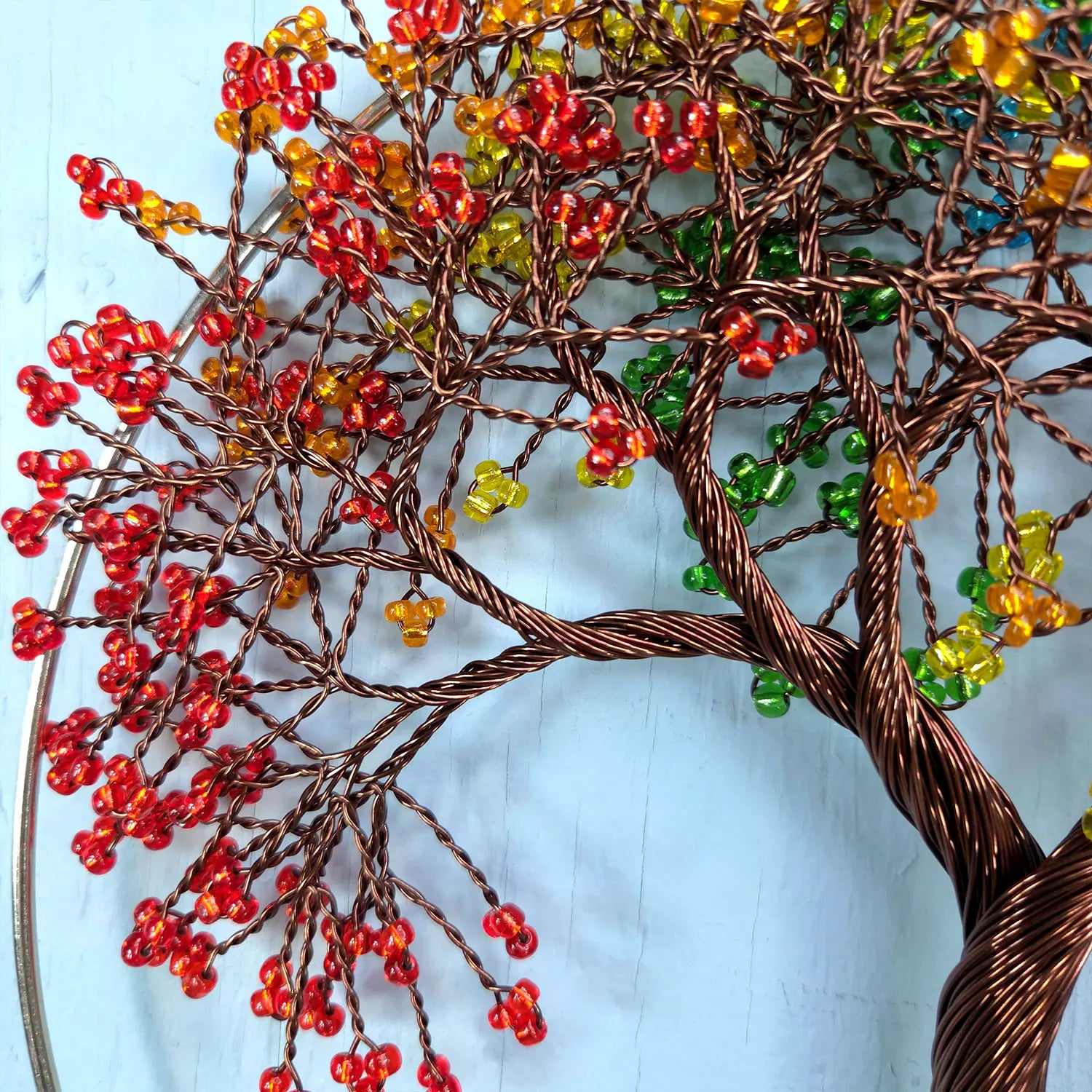 Decorative tree sculpture with red, orange, and green beads on a light blue background