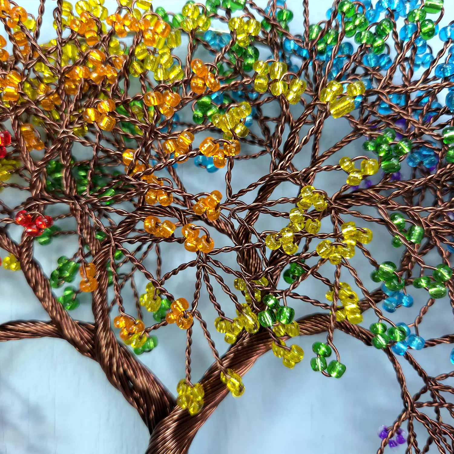 Colorful beaded tree sculpture with multicolored beads on a light blue background