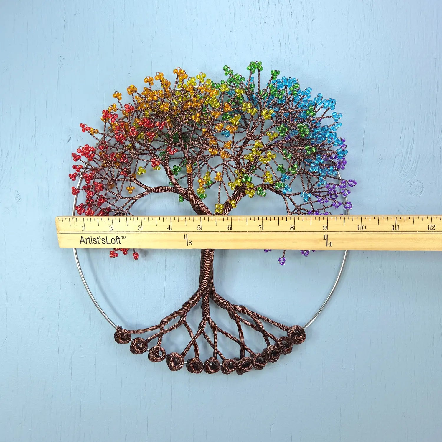Colorful beaded tree of life with a ruler for scale on a light blue background