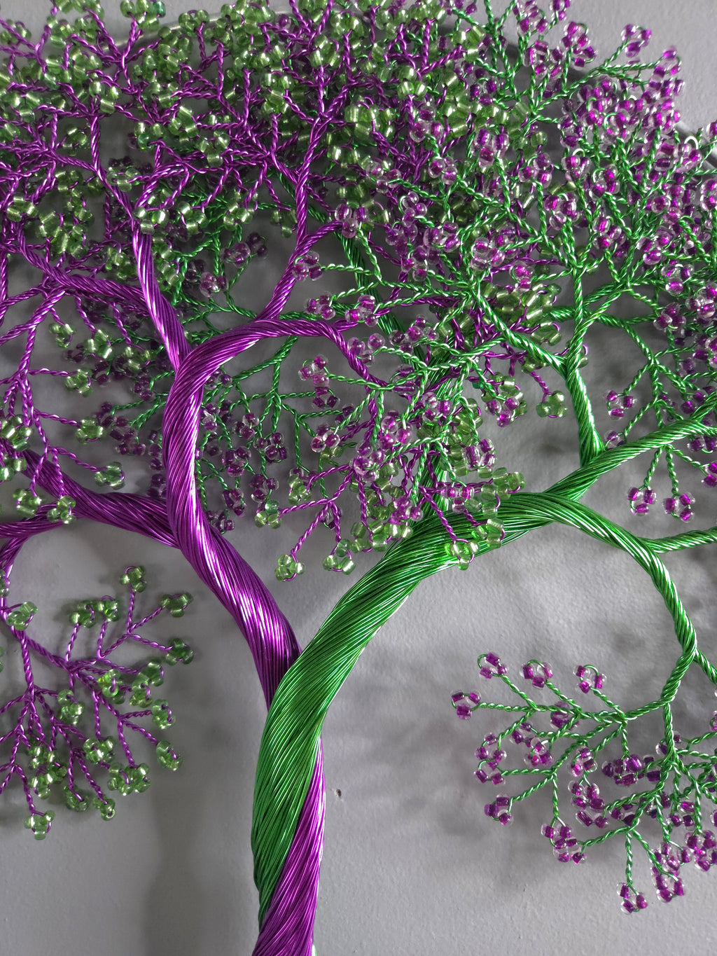 Embroidered tree design with purple and green threads on a gray background