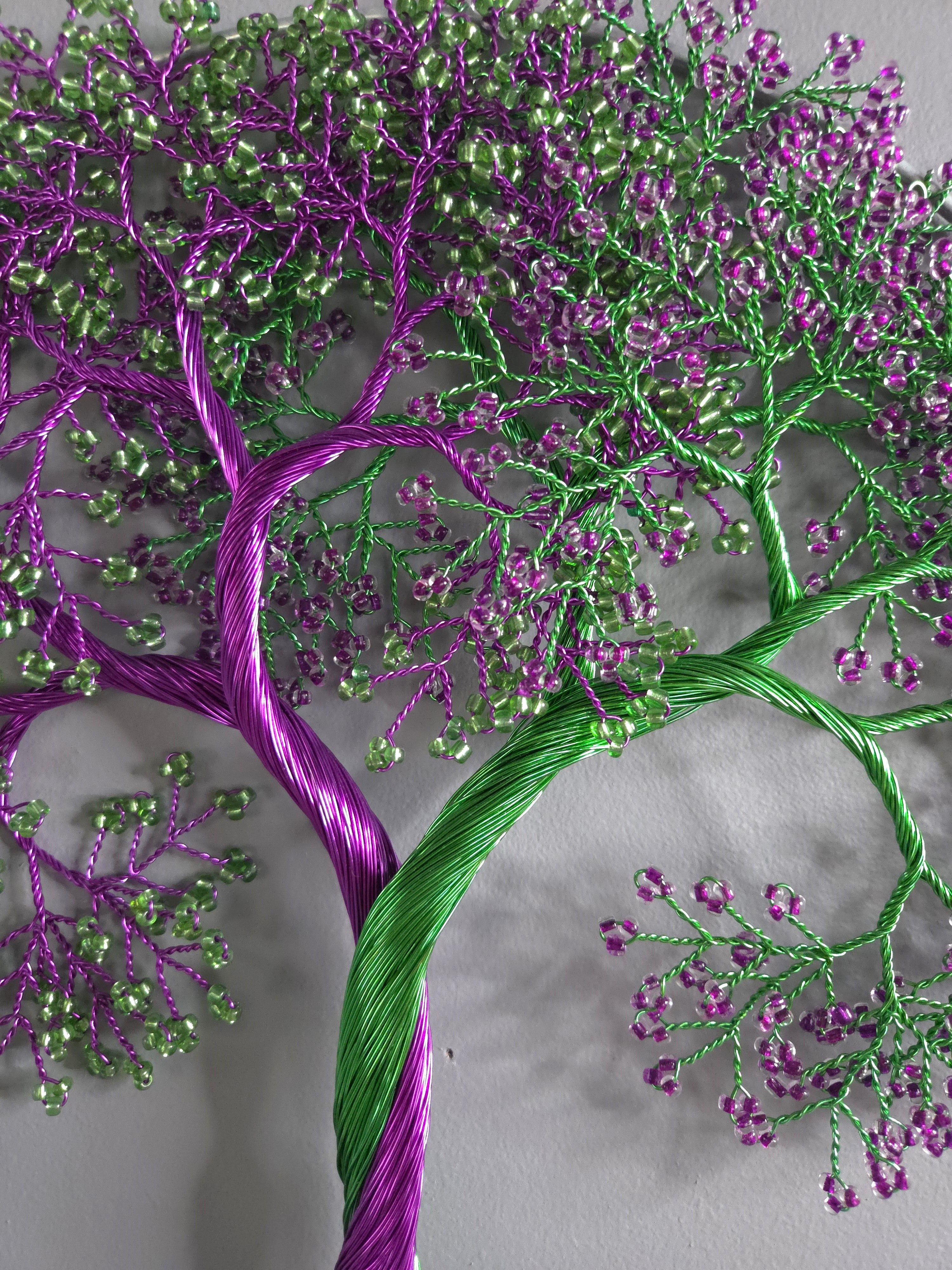 Embroidered tree design with purple and green threads on a gray background