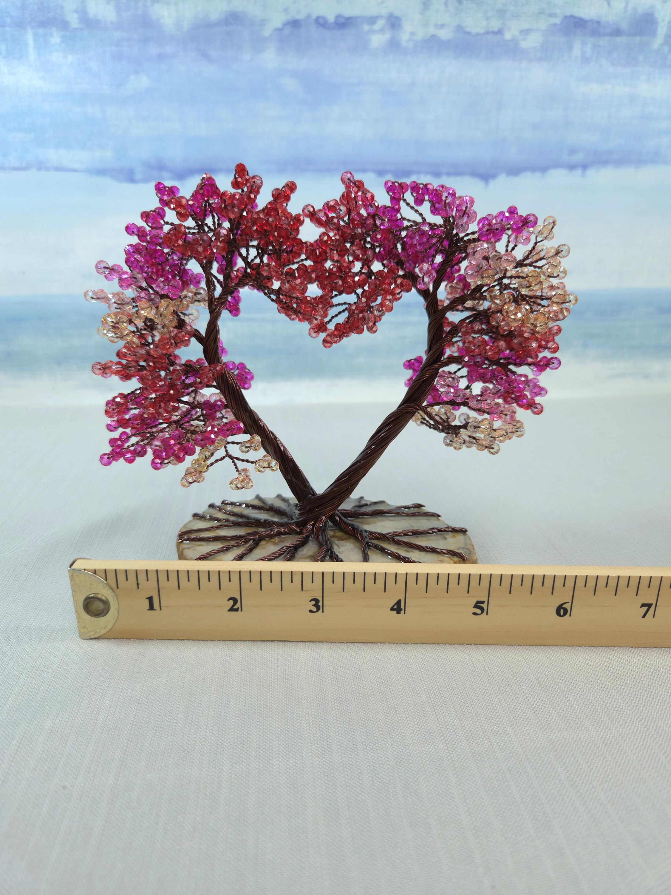 Decorative tree with pink and red beads on a white surface with a ruler for scale.