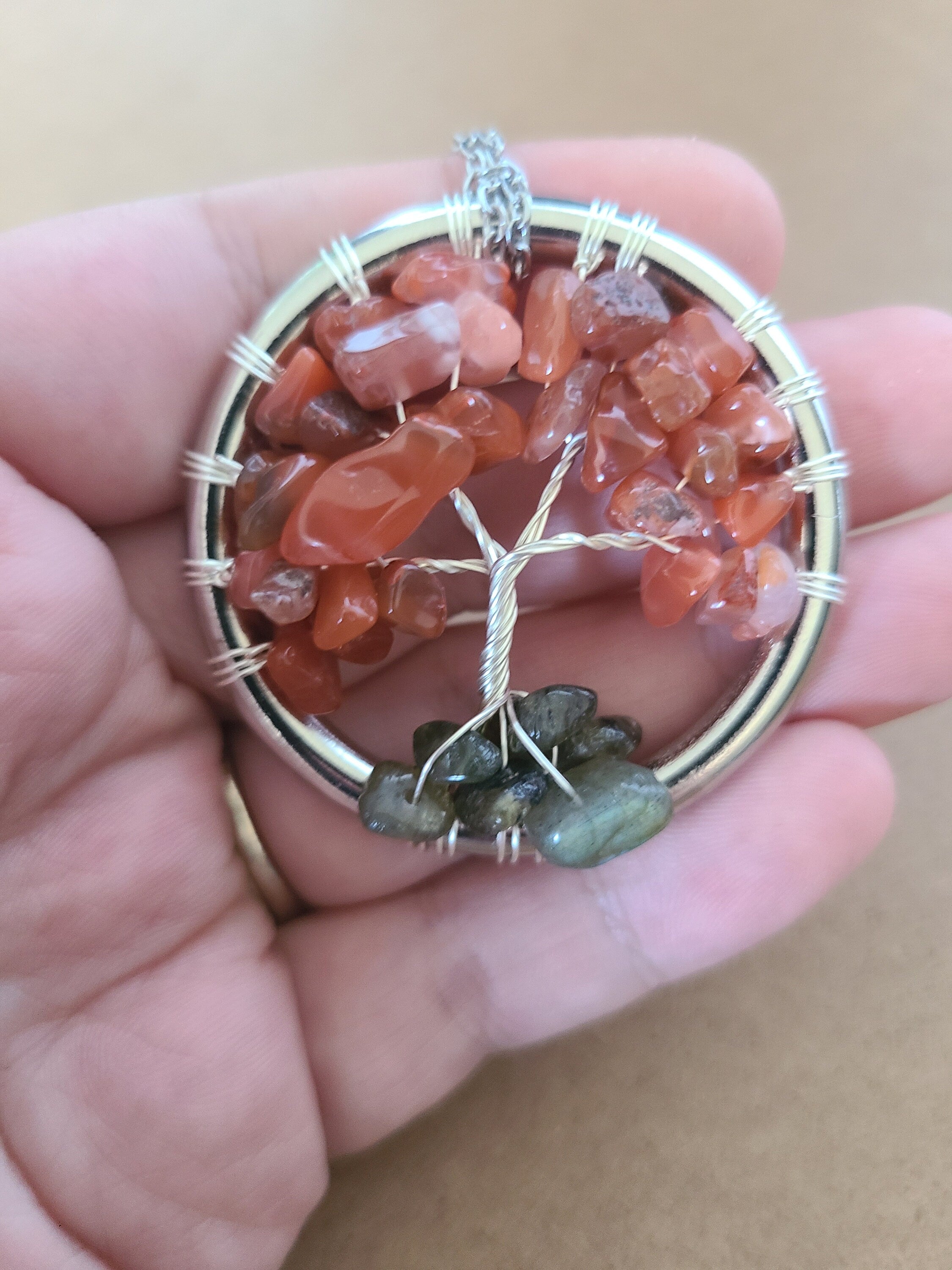 Tree of Life pendant with red stones held in a hand against a beige background