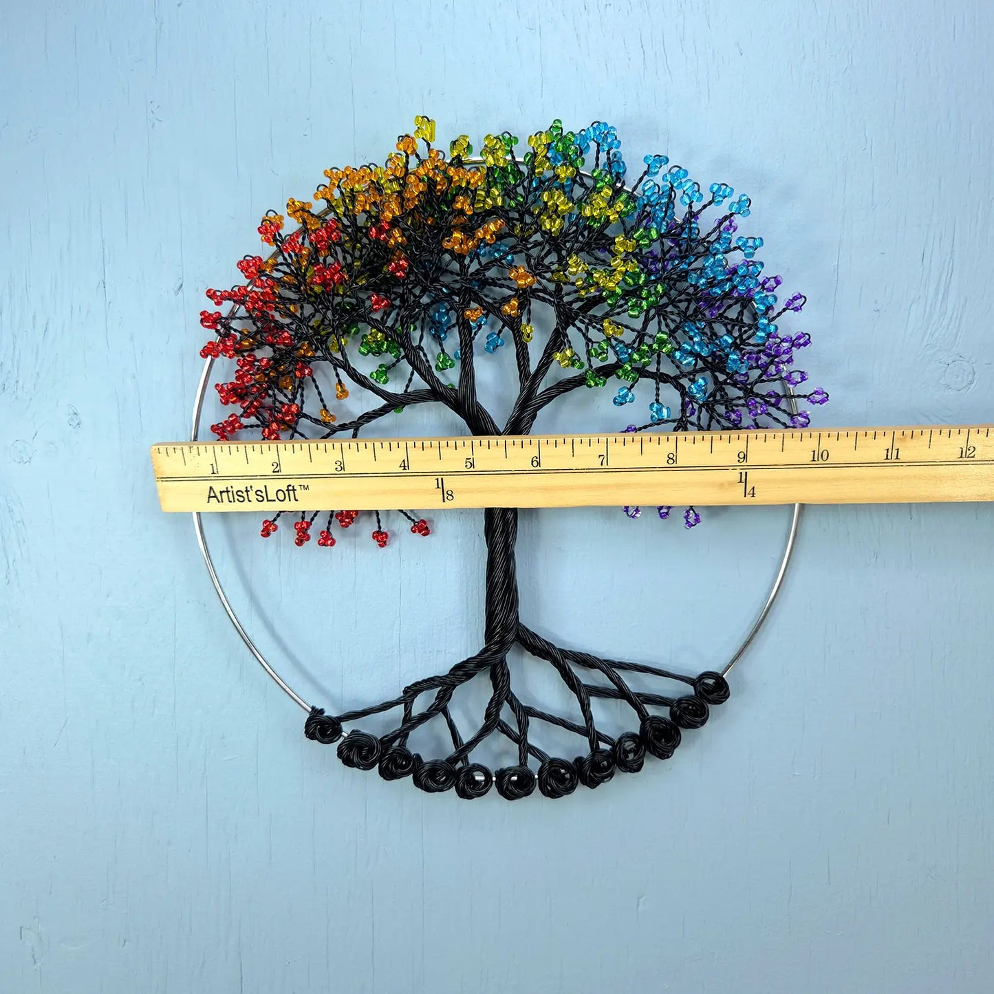 Colorful beaded tree of life with a ruler for scale on a light blue background