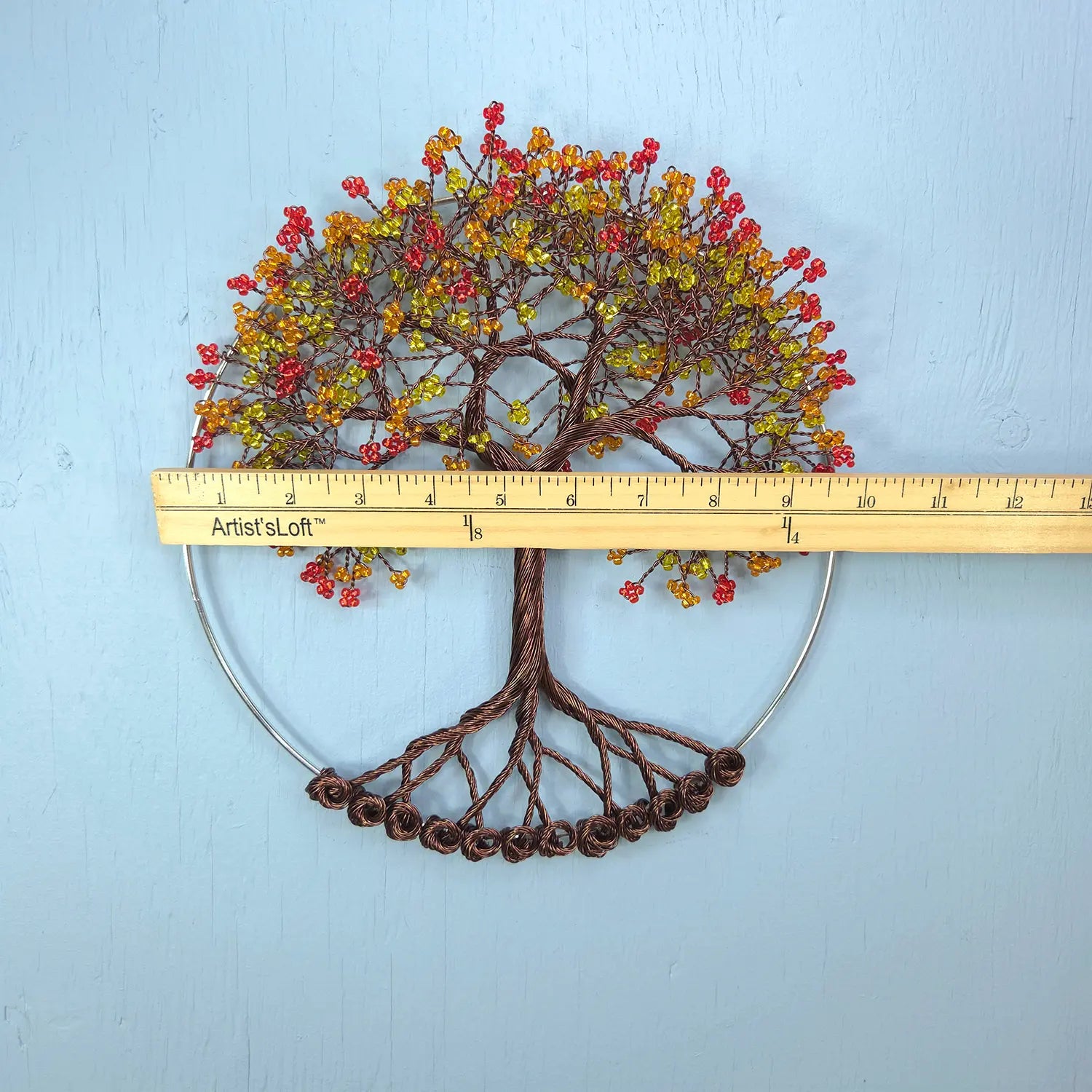 Decorative wall art of a tree with autumn leaves and roots, measured against a ruler on a light blue background.