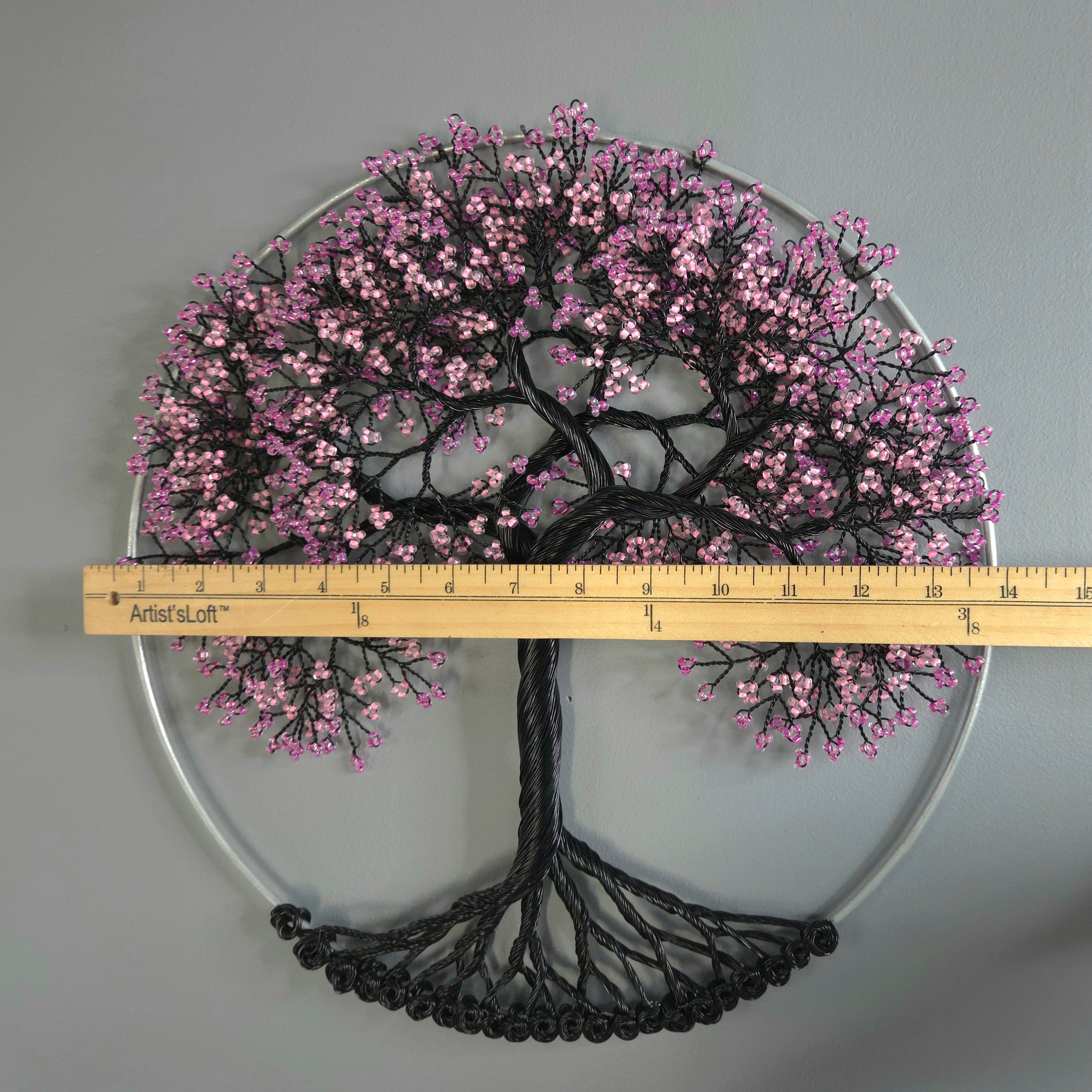 Decorative tree wall art with pink blossoms and a ruler for scale on a gray background