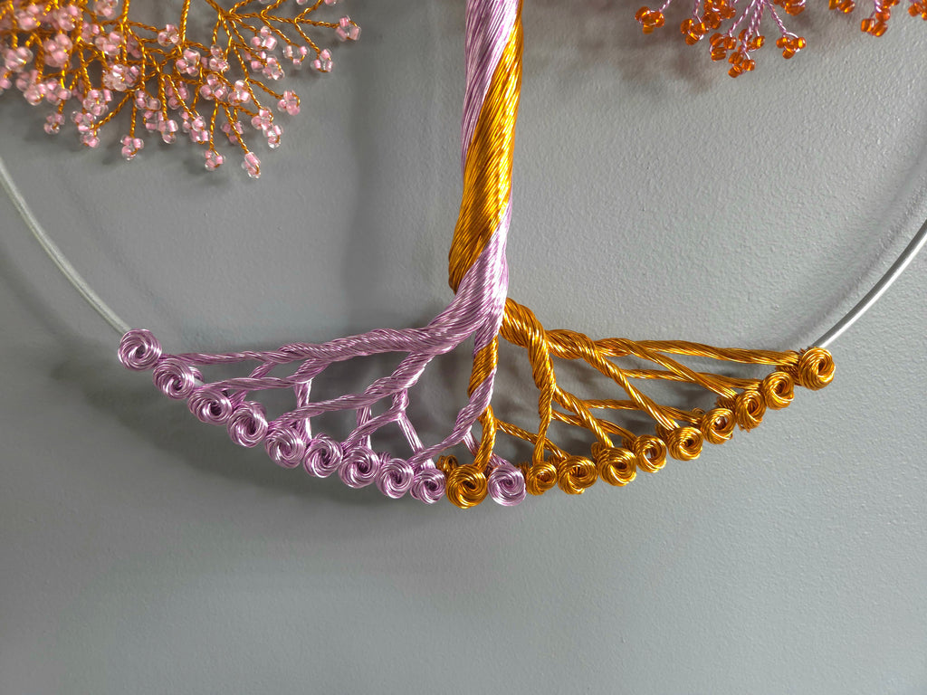Close-up of a decorative wreath with pink and gold beaded branches on a light gray background.