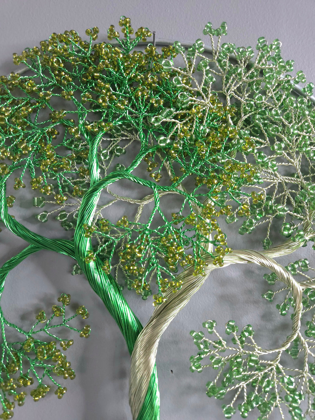 Decorative wall art of a tree with green and gold beads on a gray background