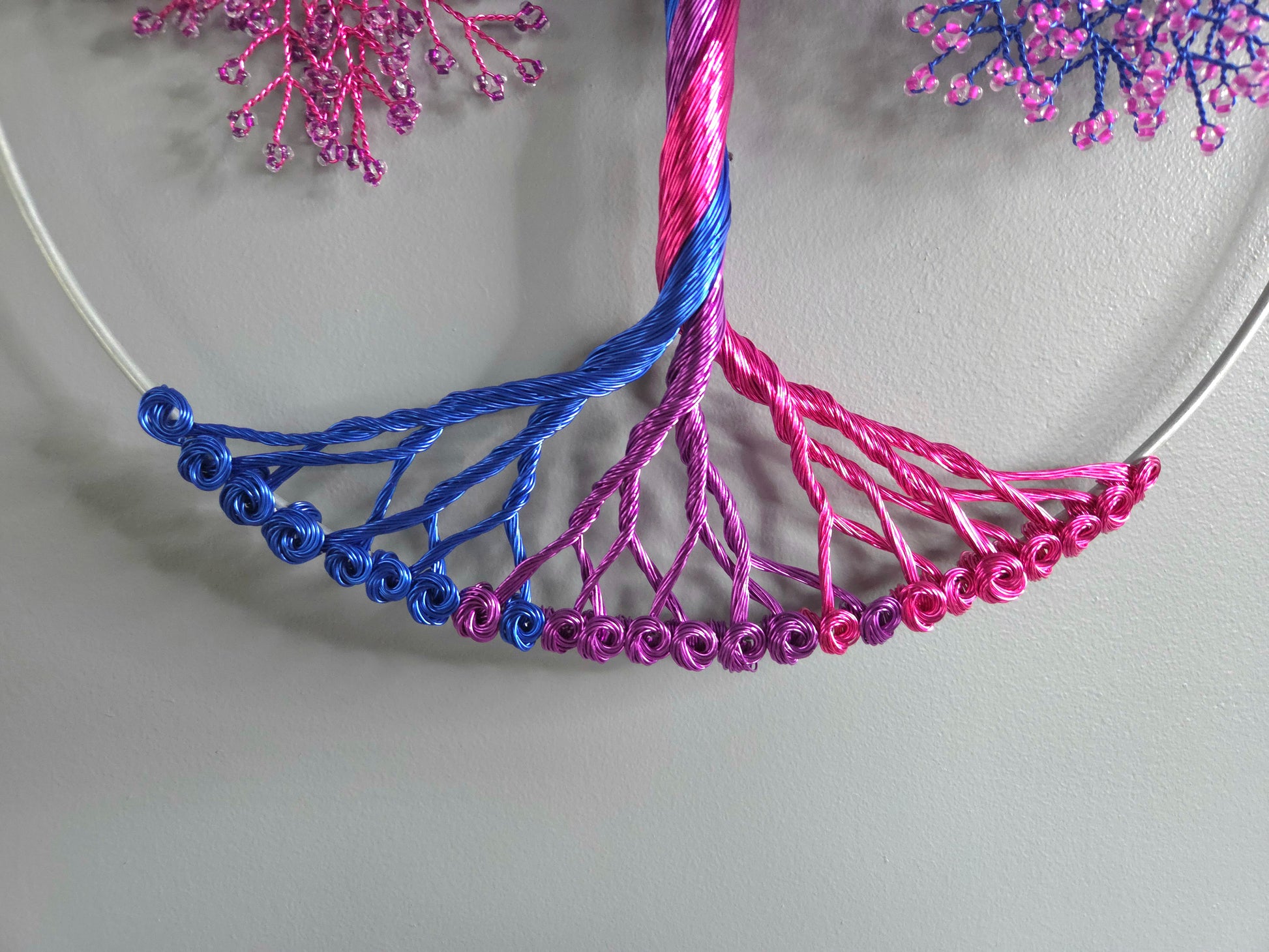 Decorative wall art of a tree with pink and blue branches on a light gray background