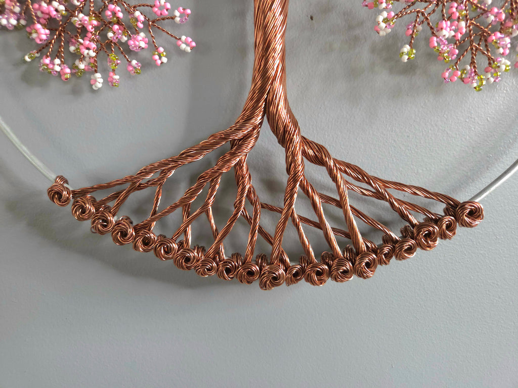 Copper wire tree sculpture with pink floral elements on a gray background