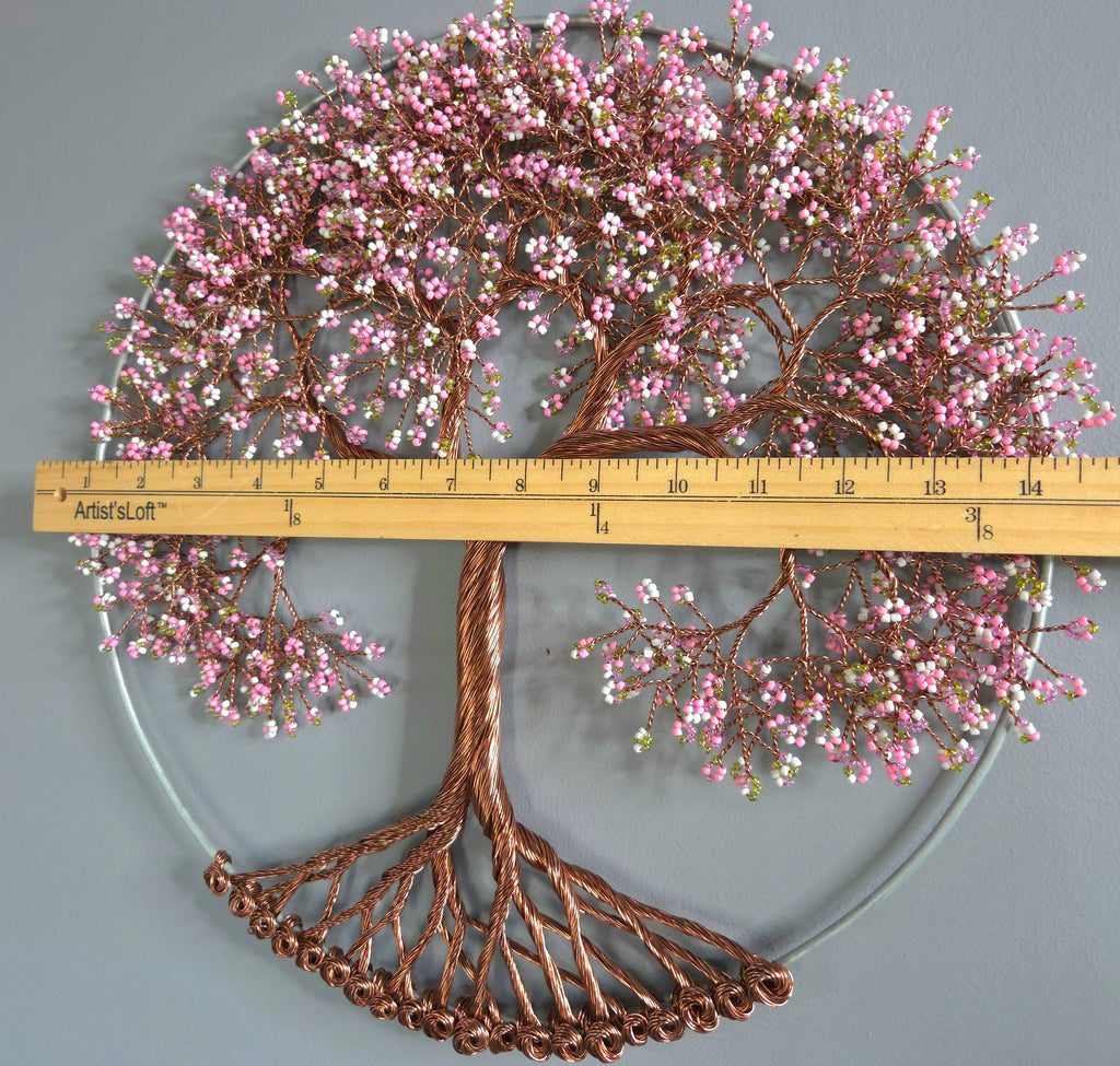 Decorative metal tree wall art with pink flowers and a ruler for scale on a gray background