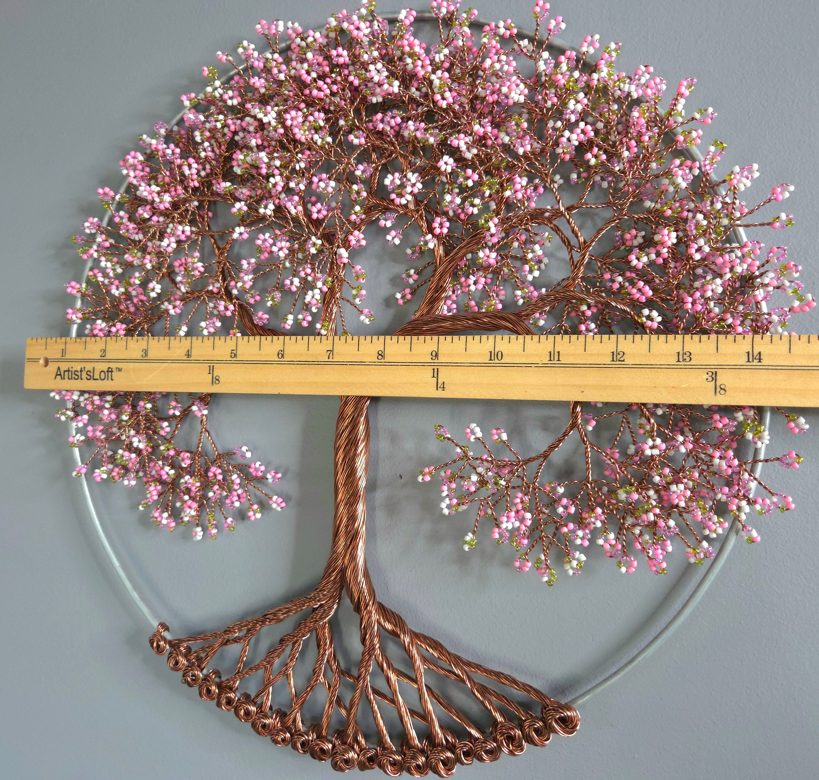 Decorative metal tree wall art with pink flowers and a ruler for scale on a gray background