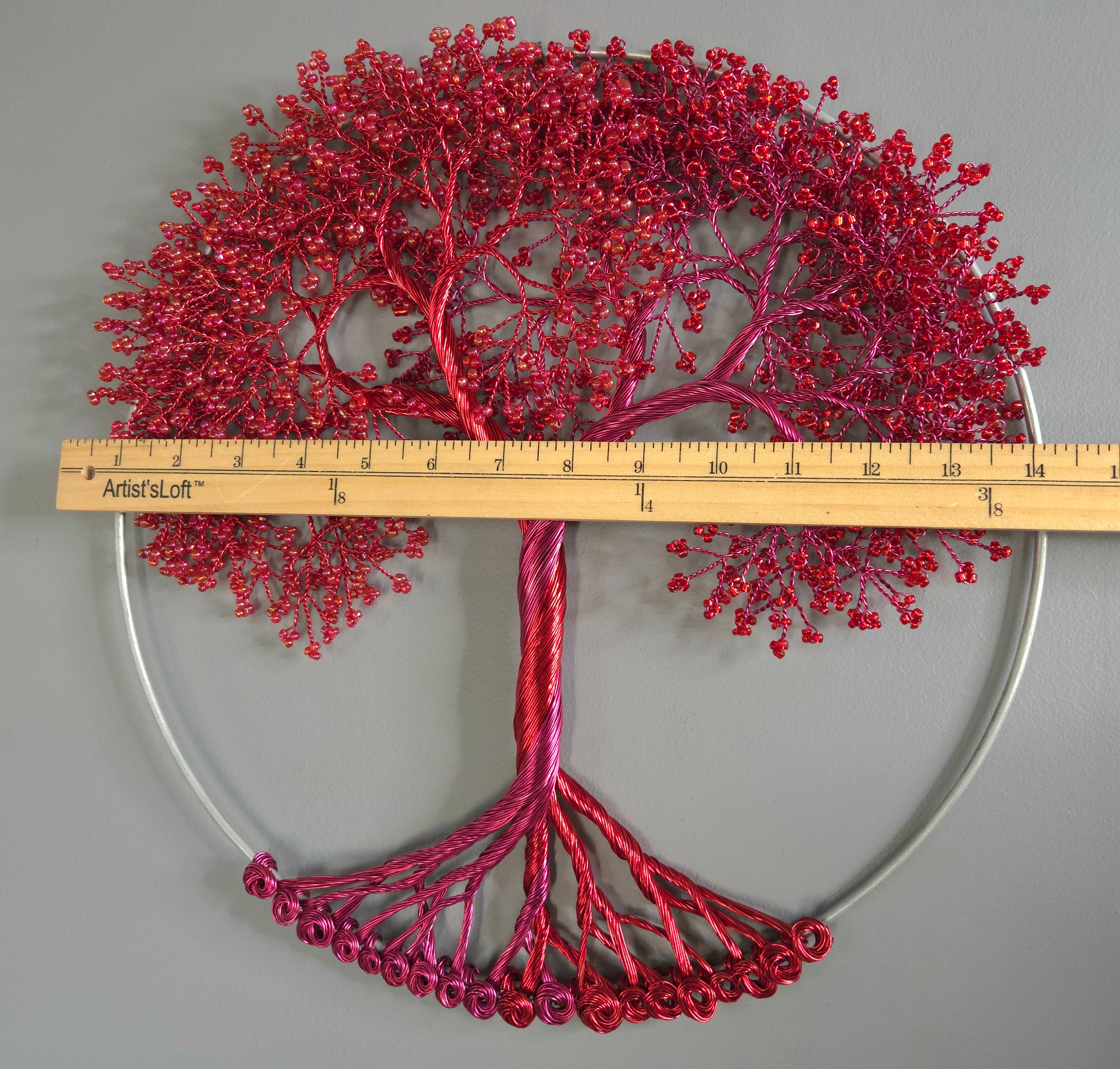 Decorative red tree sculpture with a ruler for scale on a gray background