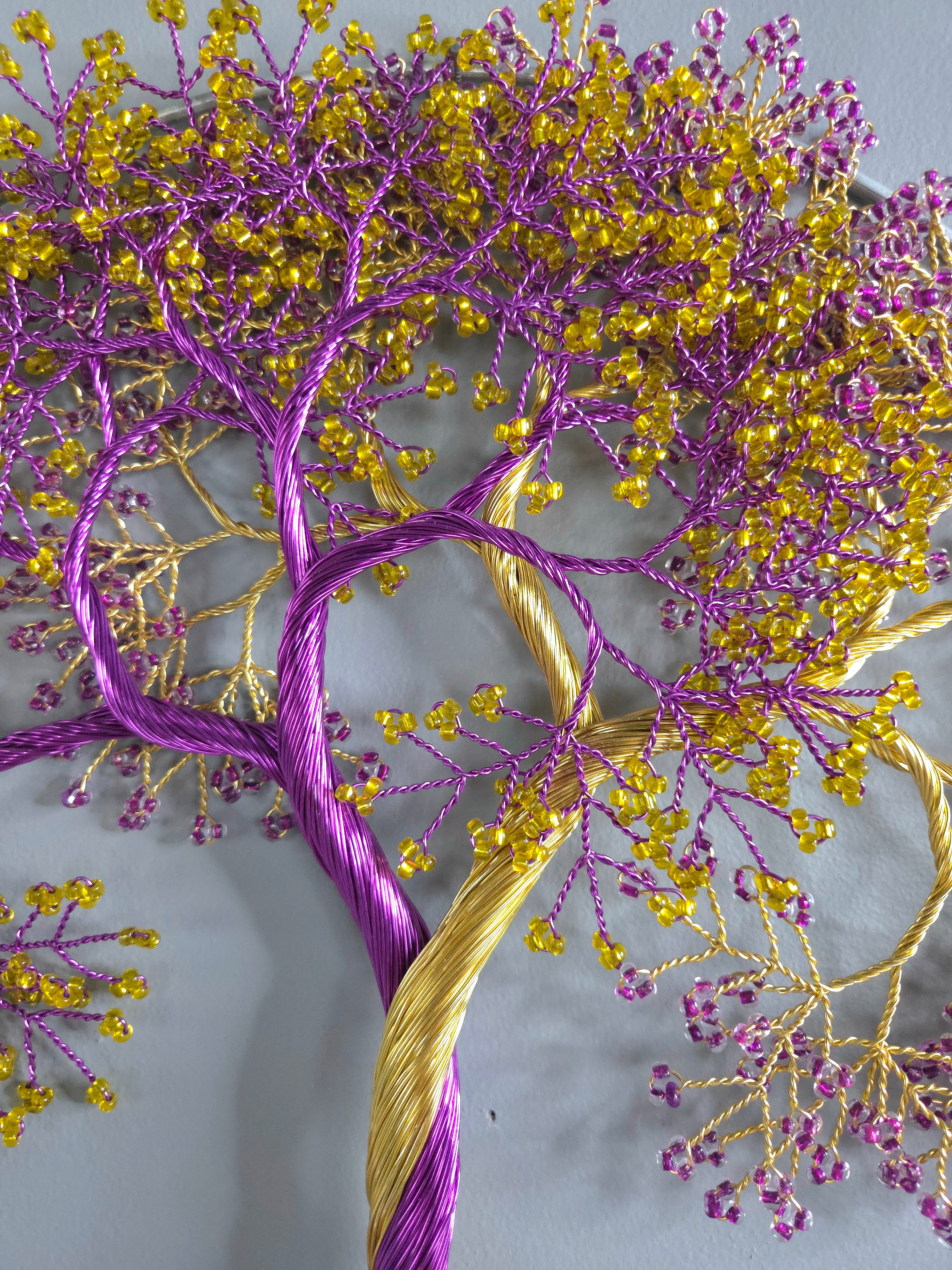 Embroidered tree design with purple and gold threads on a gray background