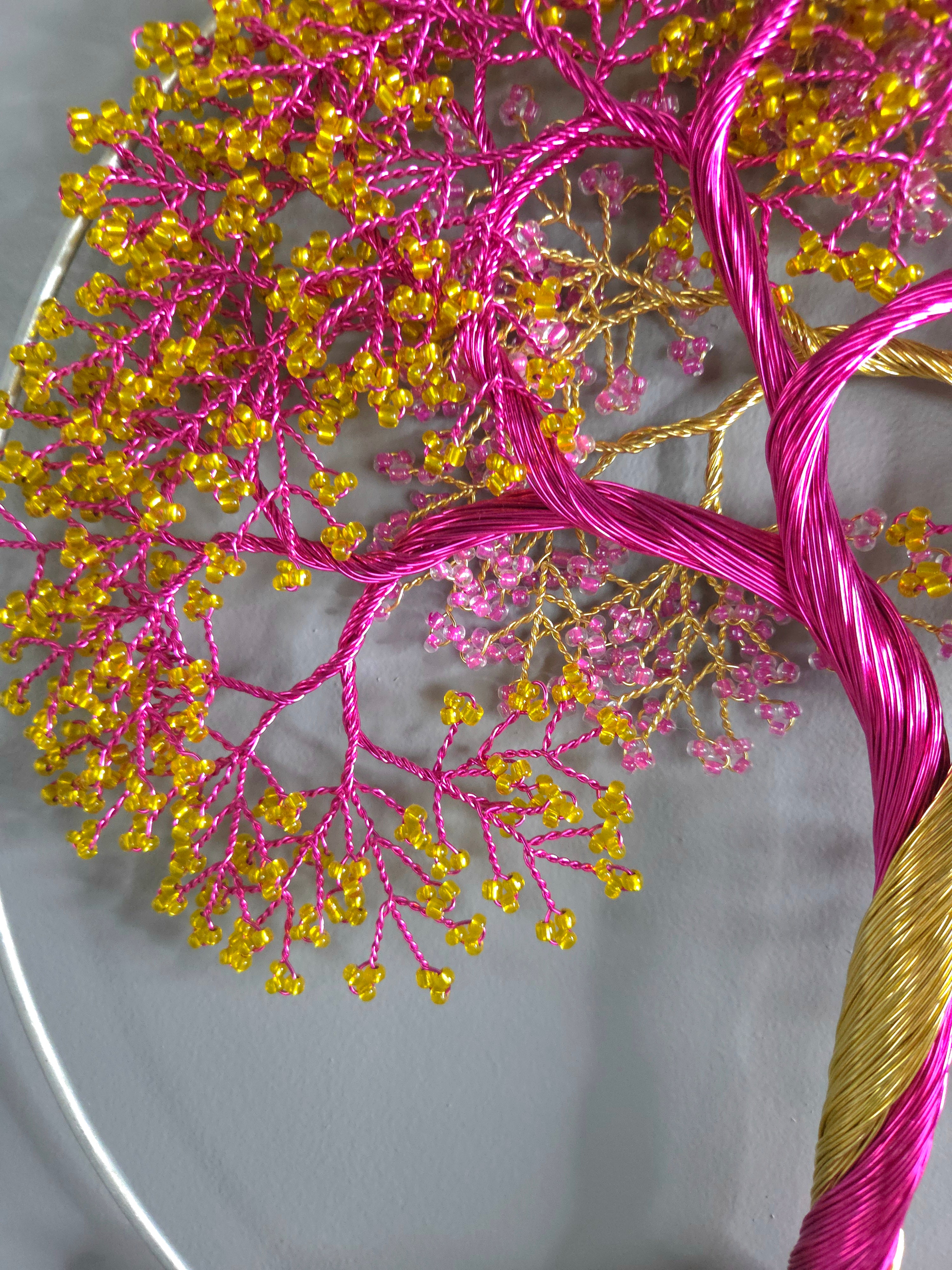 Embroidery hoop with pink and yellow thread tree design on a white background