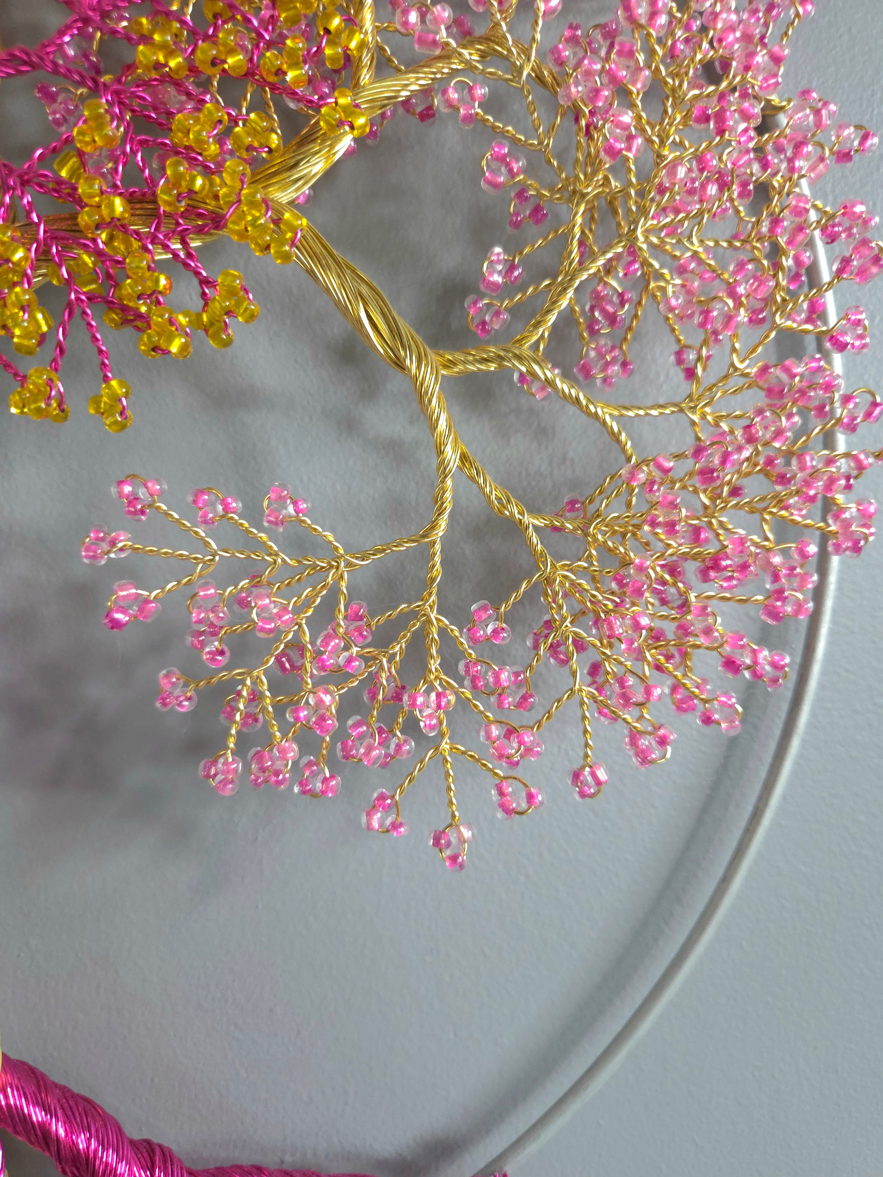 Embroidery hoop with pink and gold bead tree design on a gray background