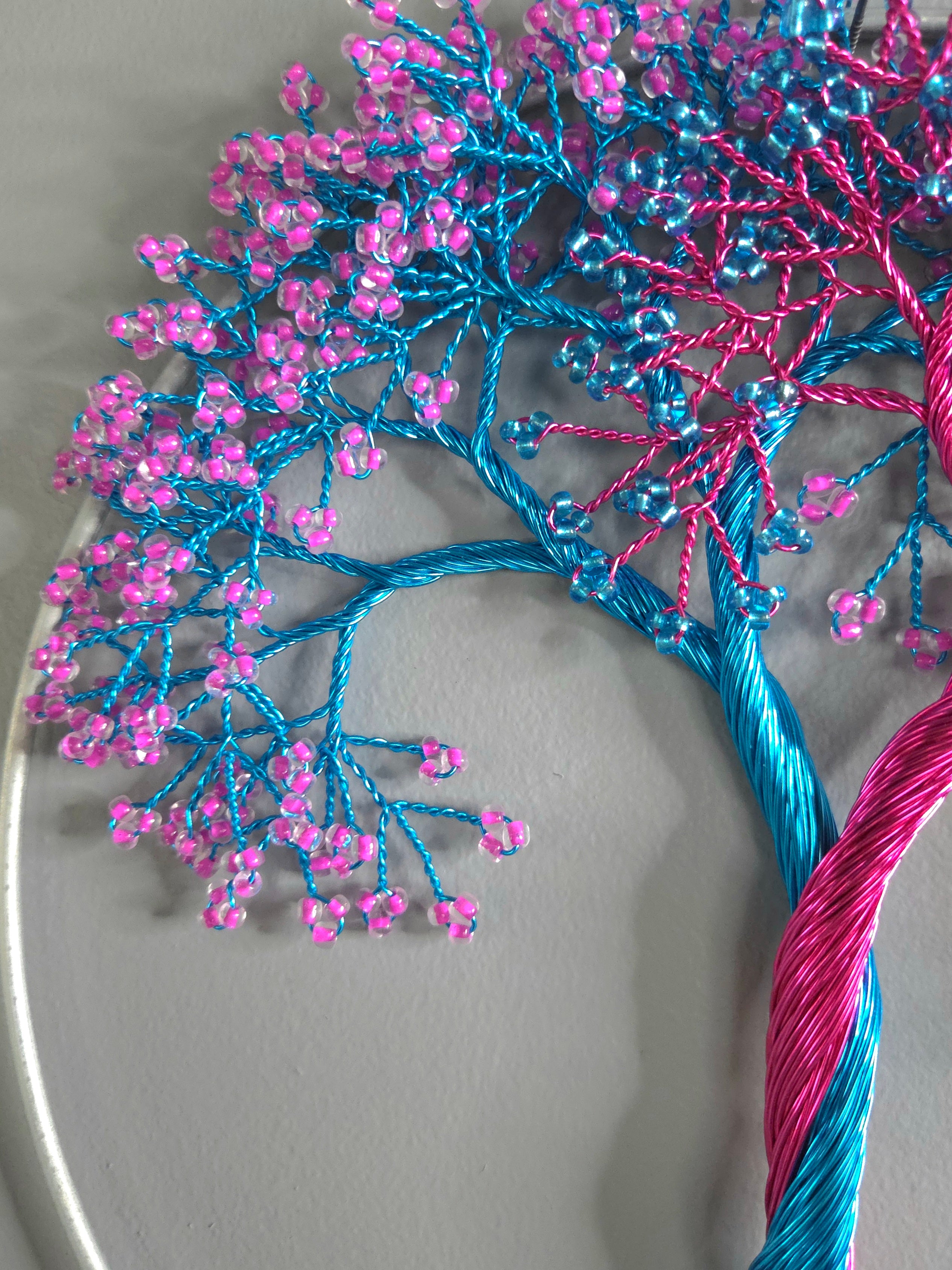 Decorative branch with blue and pink yarn and beads on a gray background