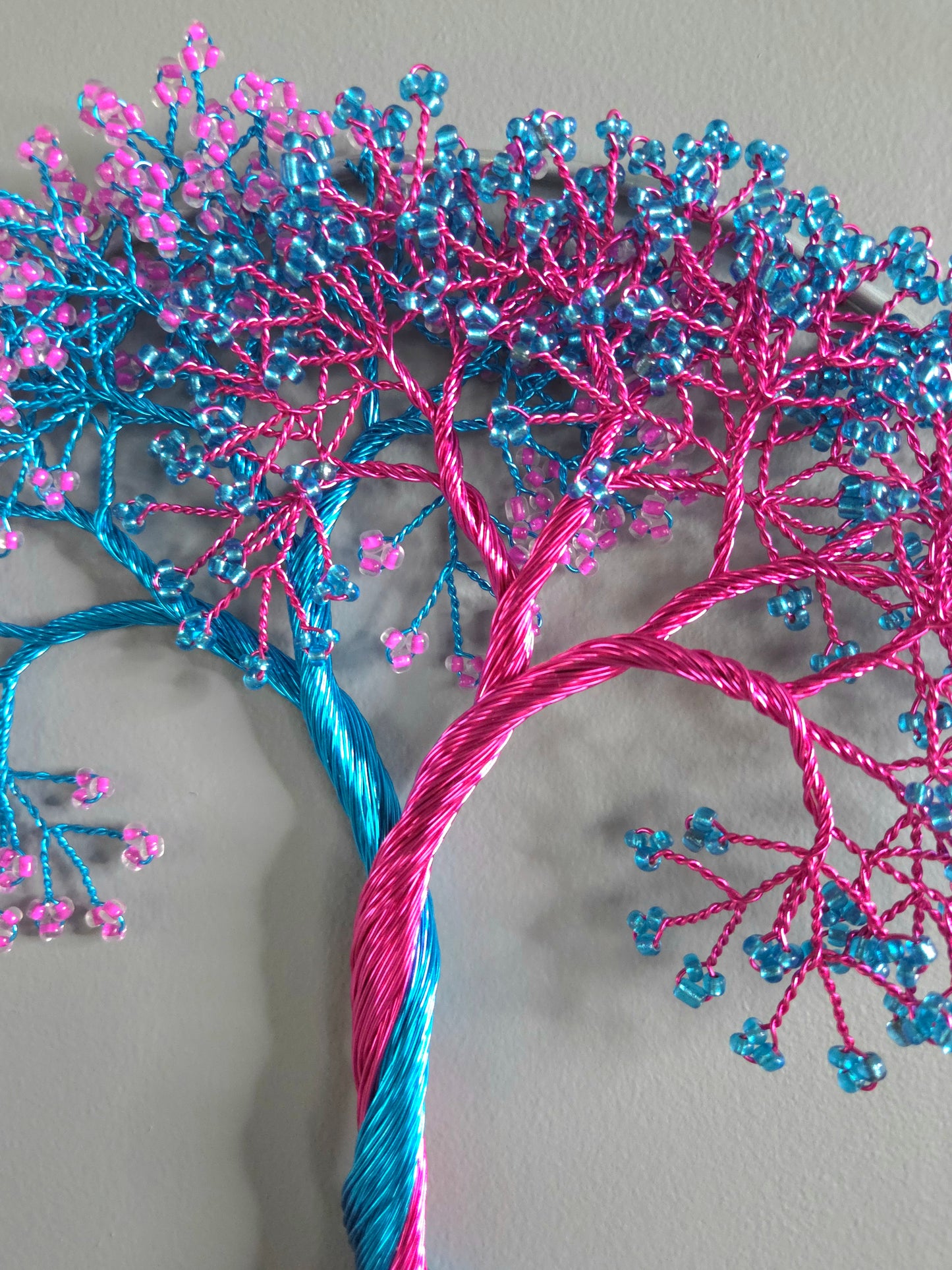 Decorative wall art of a tree made from blue and pink yarn on a plain background