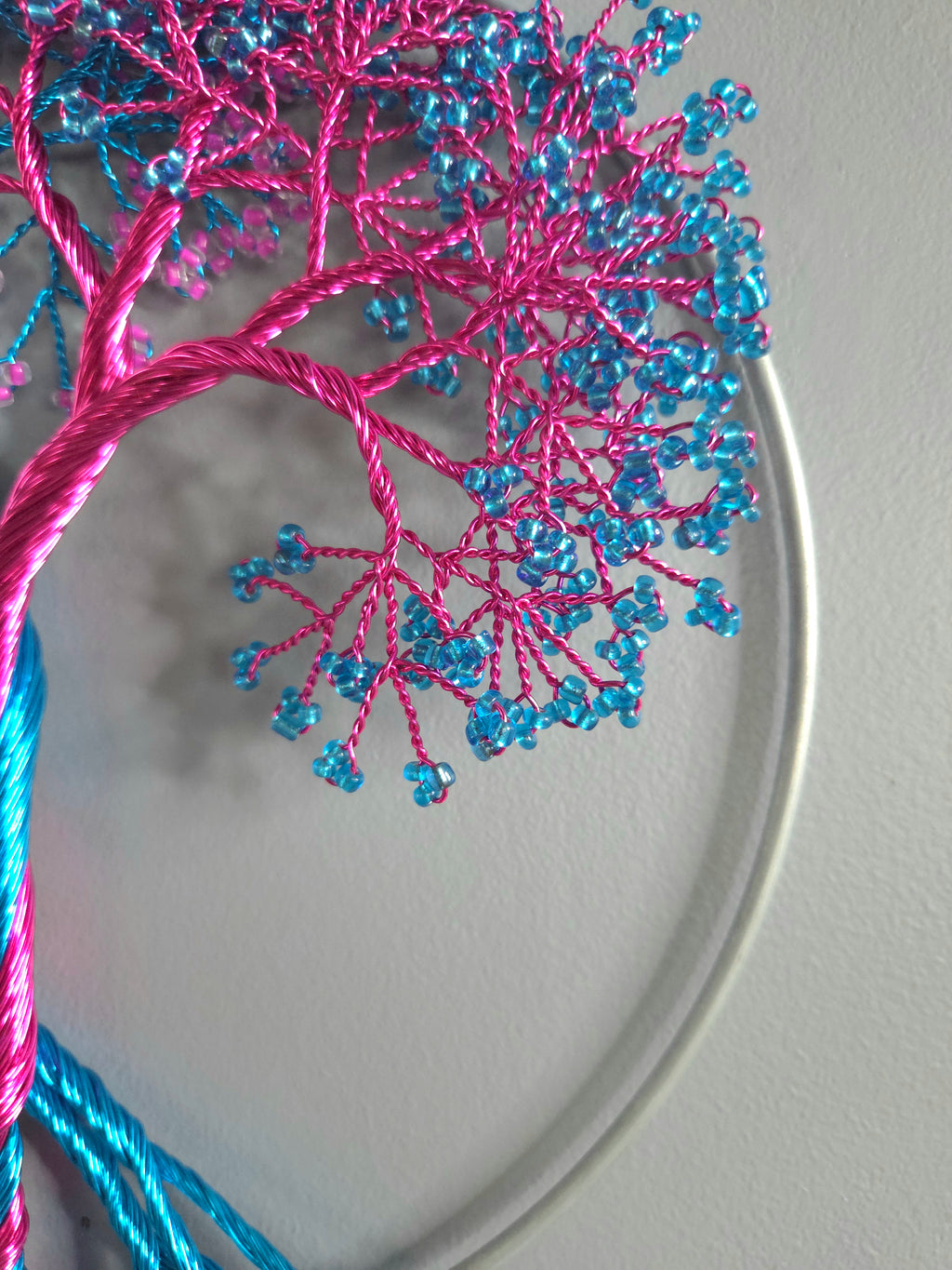 Embroidery hoop with pink and blue thread tree design on a plain background