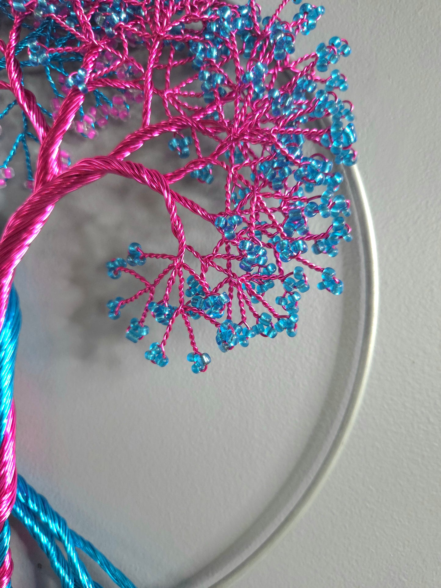 Embroidery hoop with pink and blue thread tree design on a plain background