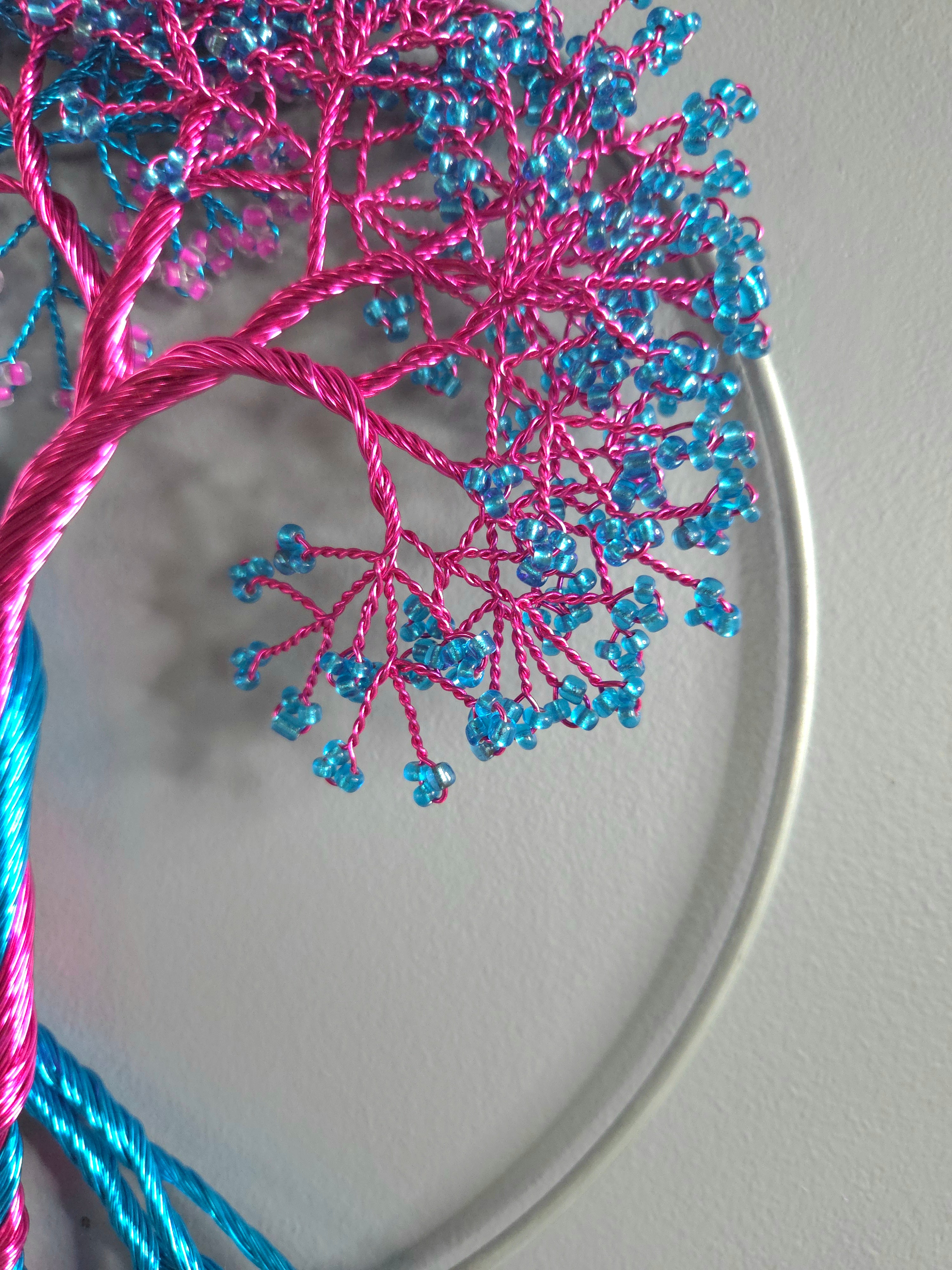 Embroidery hoop with pink and blue thread tree design on a plain background