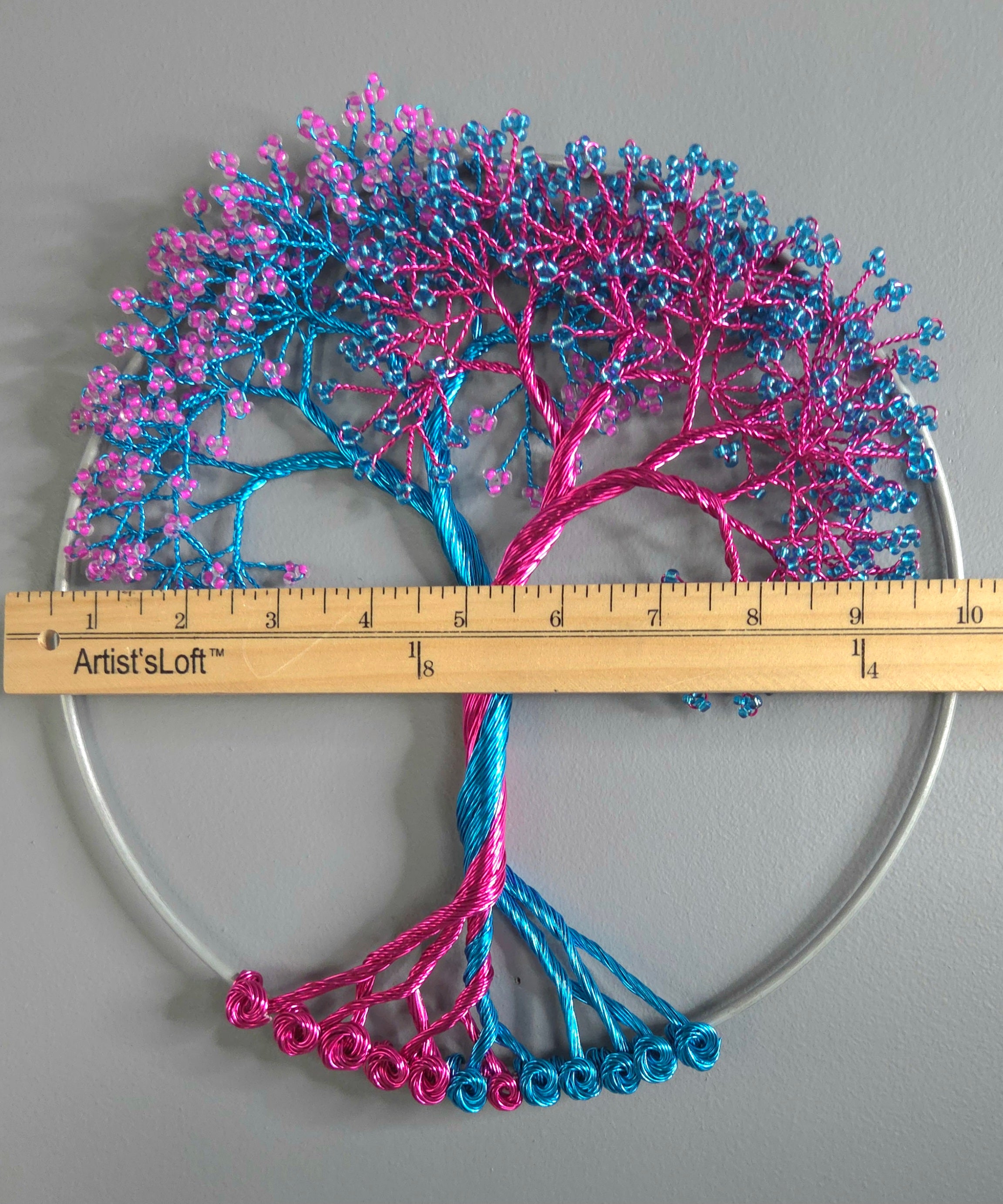 Decorative tree sculpture with pink and blue branches on a gray background, measured by a ruler.