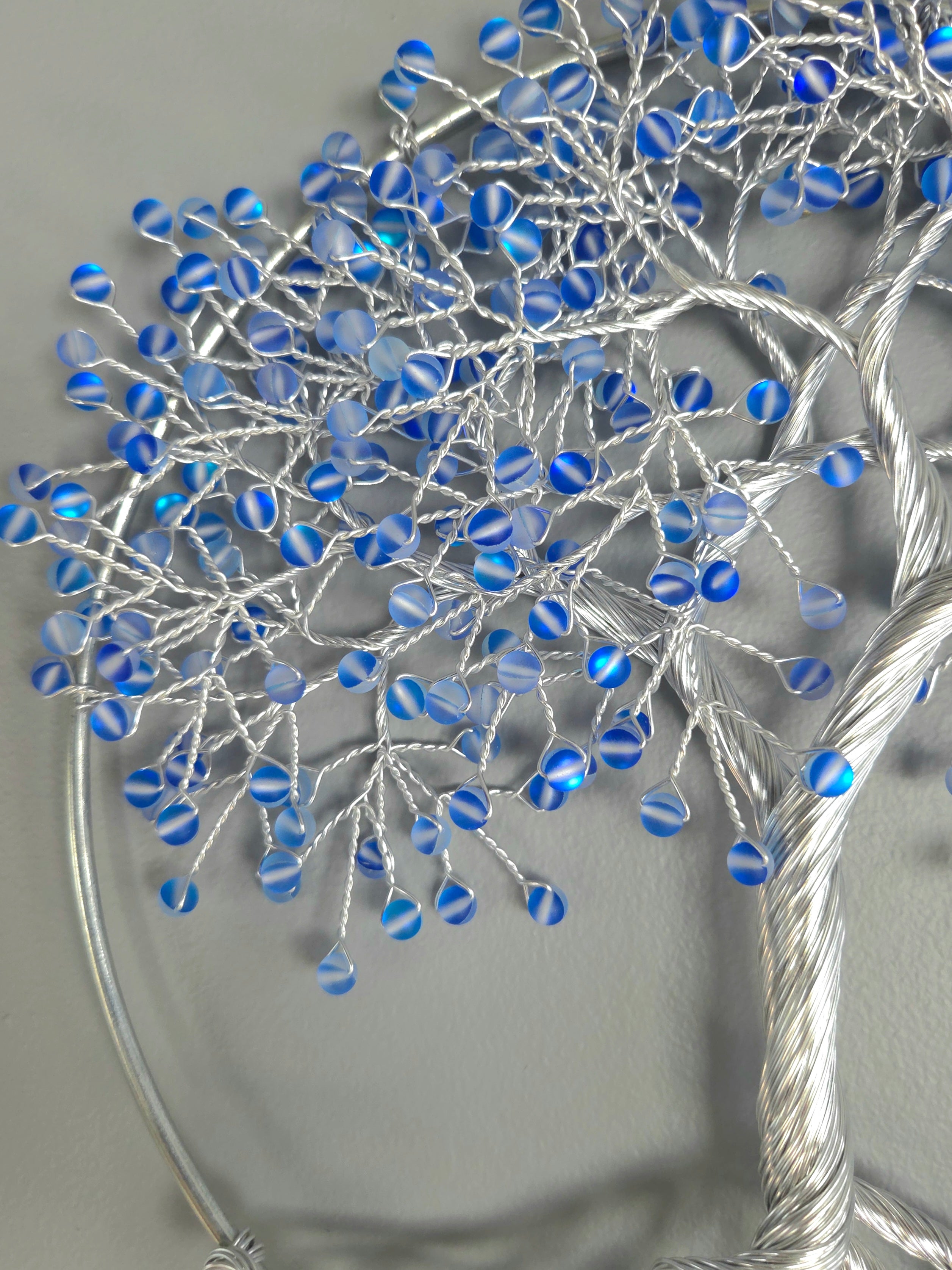 Decorative wall art of a tree with blue beads on a gray background