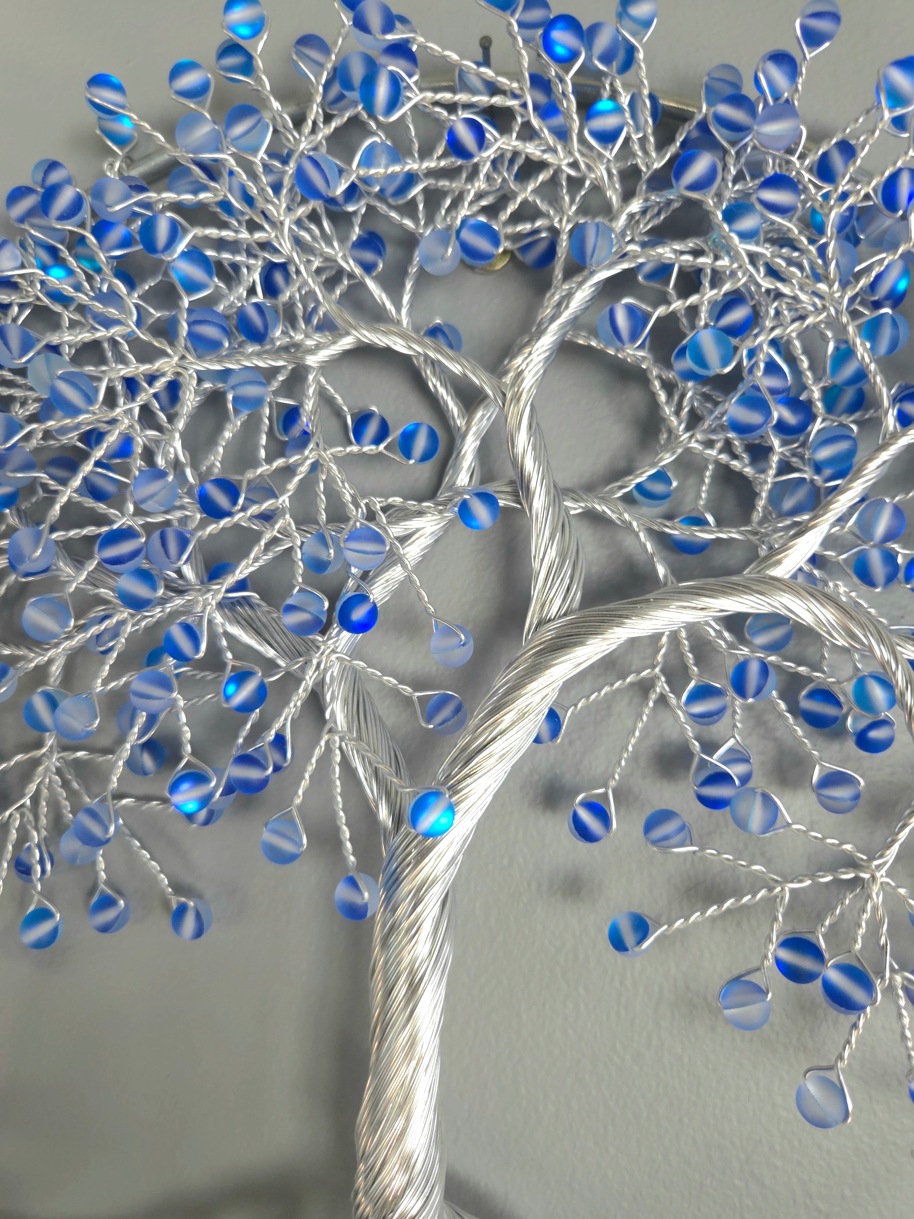 Decorative wall art of a tree with blue beads on a gray background