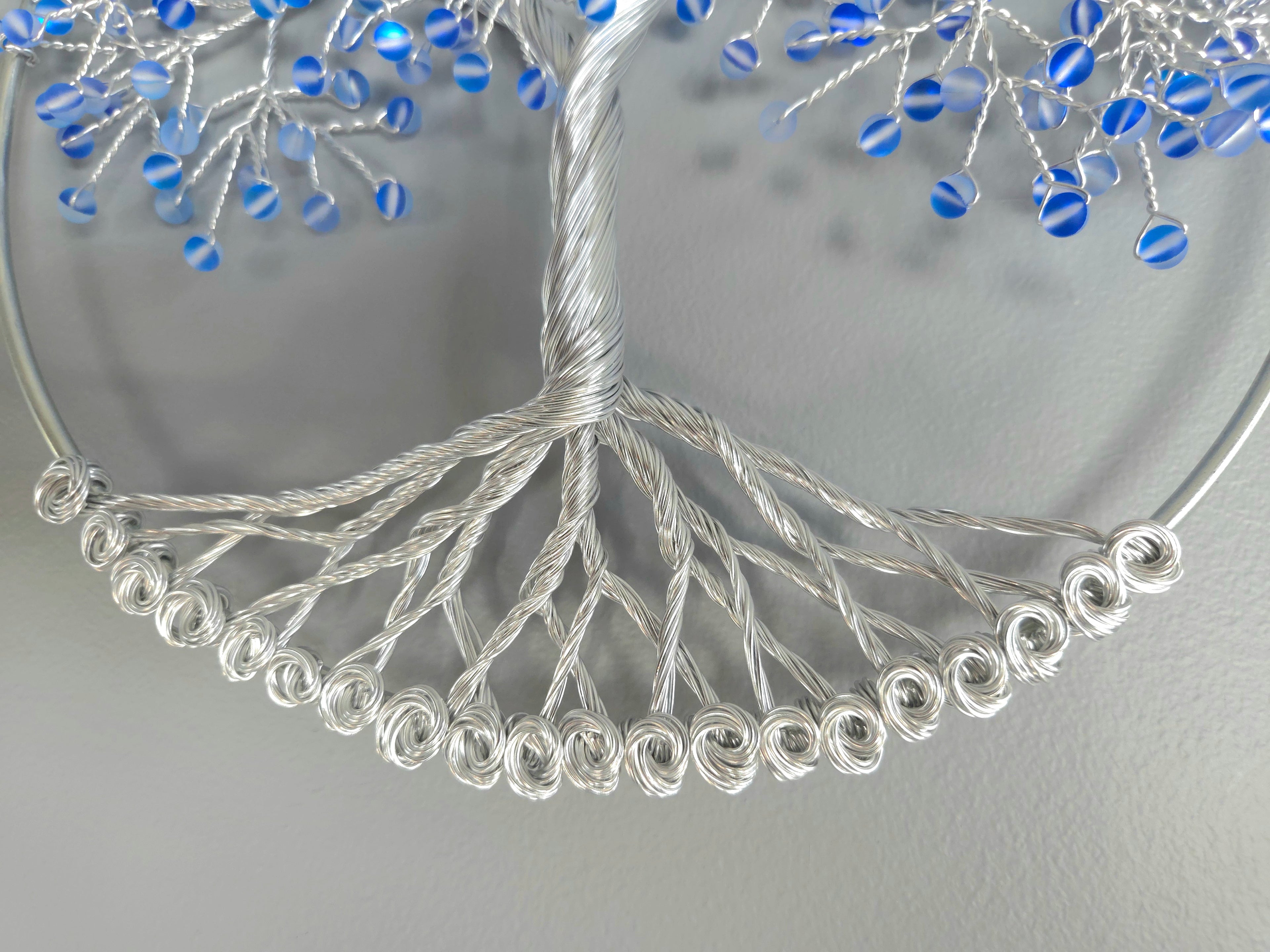 Decorative wall art of a tree with blue beads on a gray background