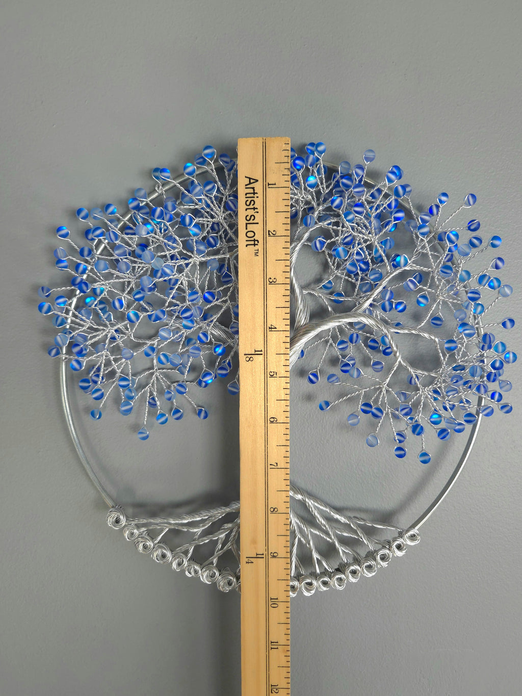 Decorative wall art of a tree with blue beads on a gray background