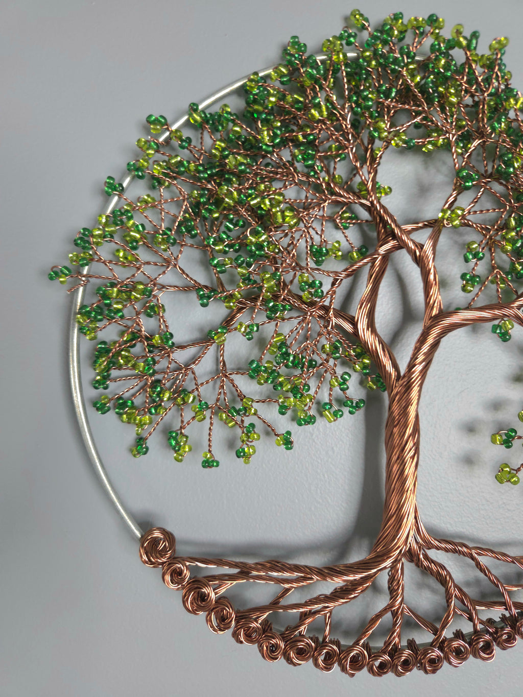 Decorative wall art of a tree with green beads and copper accents on a gray background