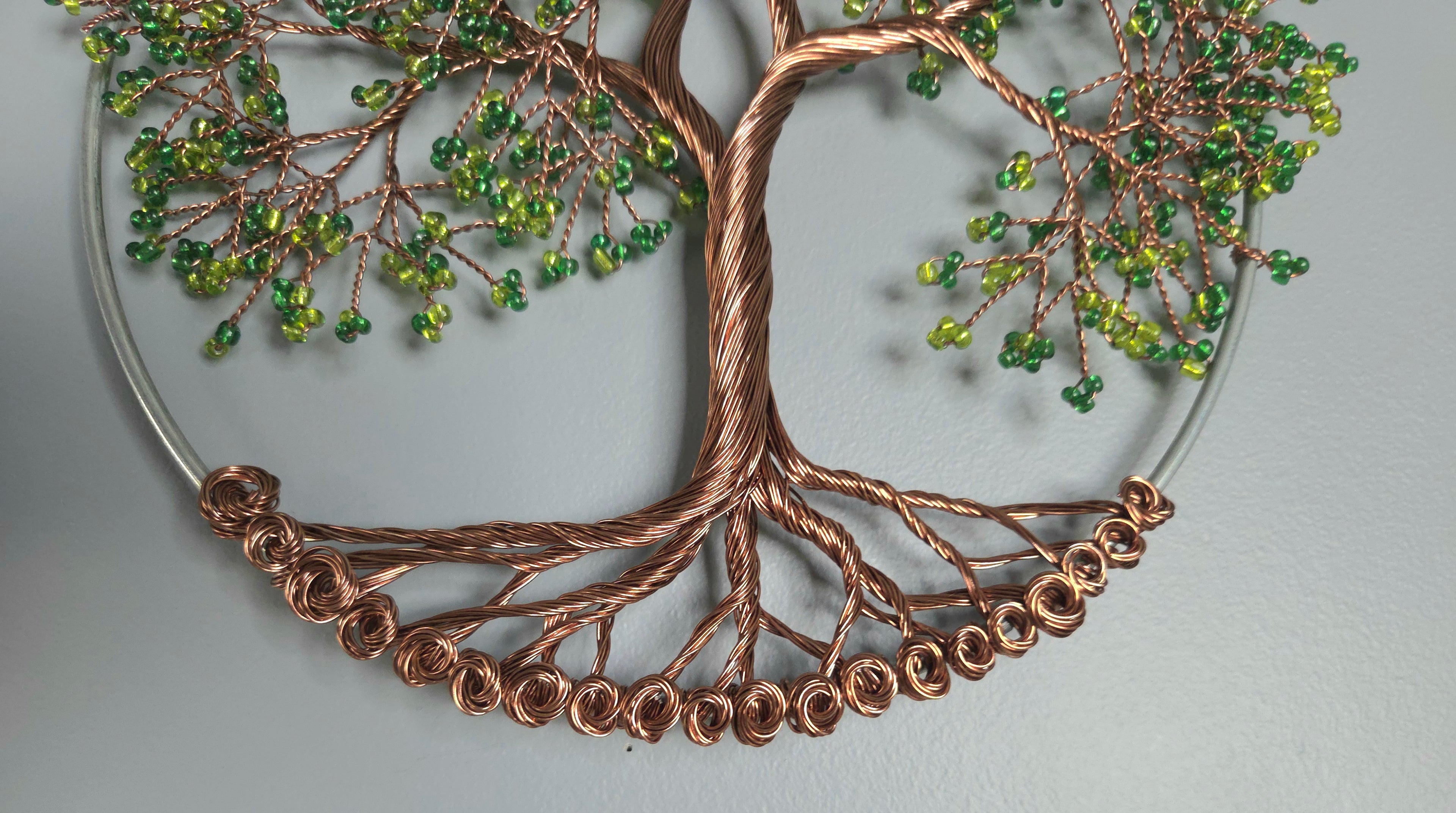 Decorative wall art of a tree with copper branches and green beads on a light gray background
