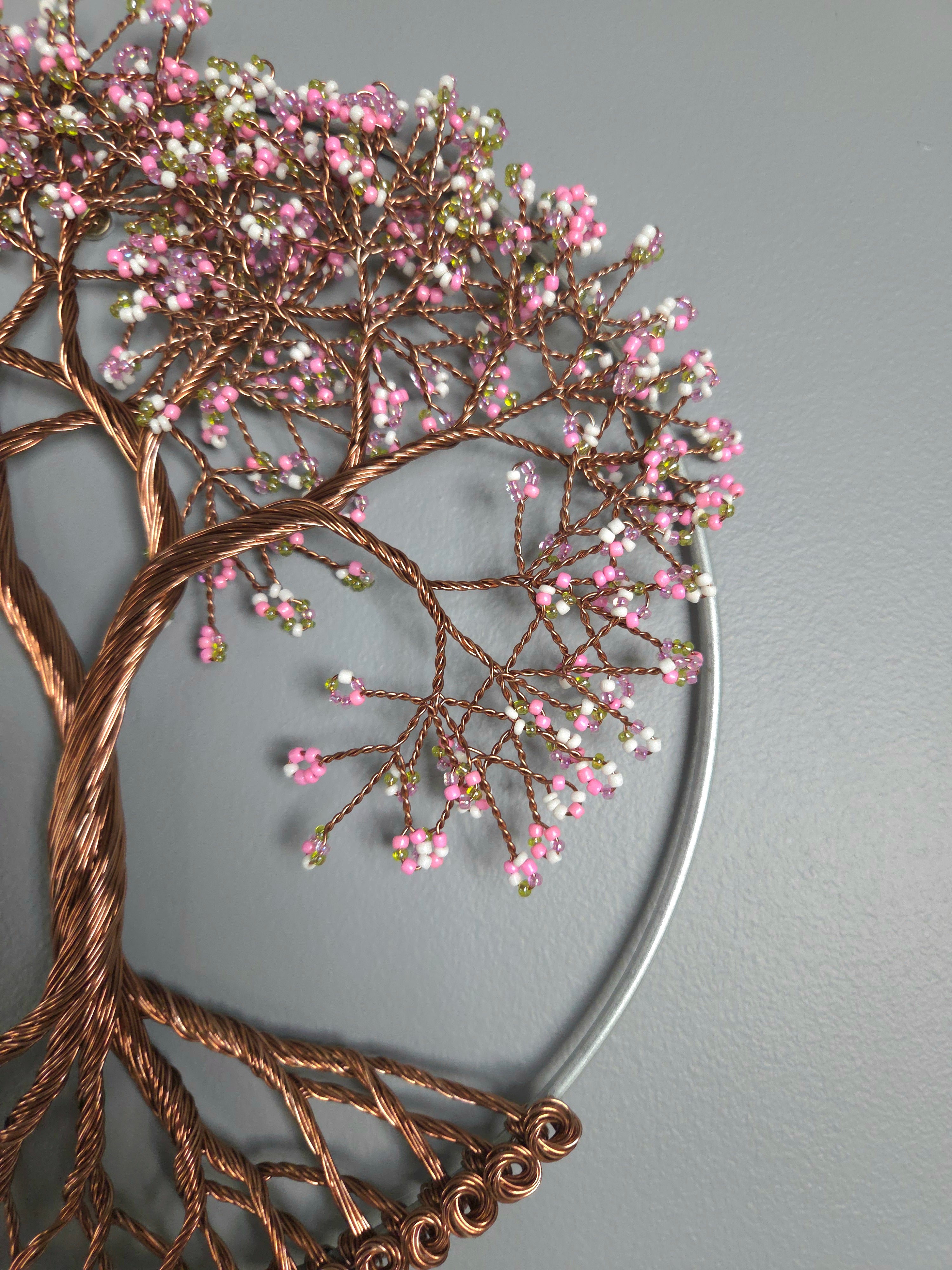 Decorative metal wall art of a tree with pink blossoms on a gray background