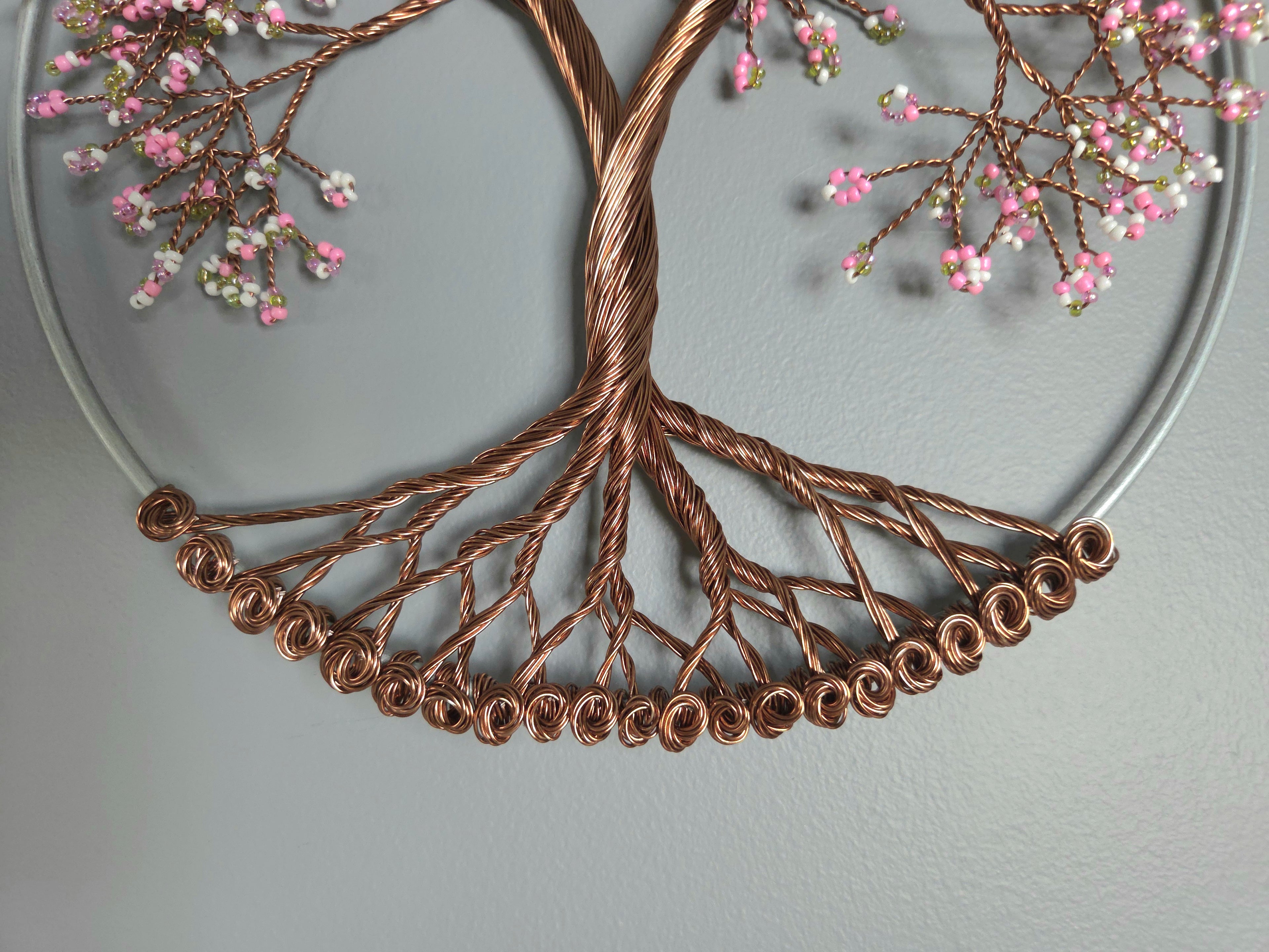 Decorative wall art in the shape of a tree with copper branches and pink flowers on a gray background