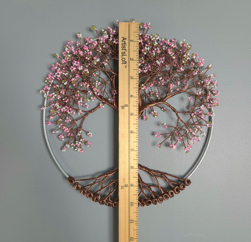 Decorative wall art in the shape of a tree with pink blossoms and brown branches, accompanied by a ruler for scale on a gray background.