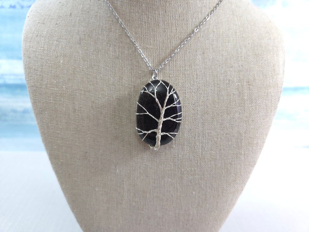 Black tree of life pendant on a silver chain displayed on a bust against a light background