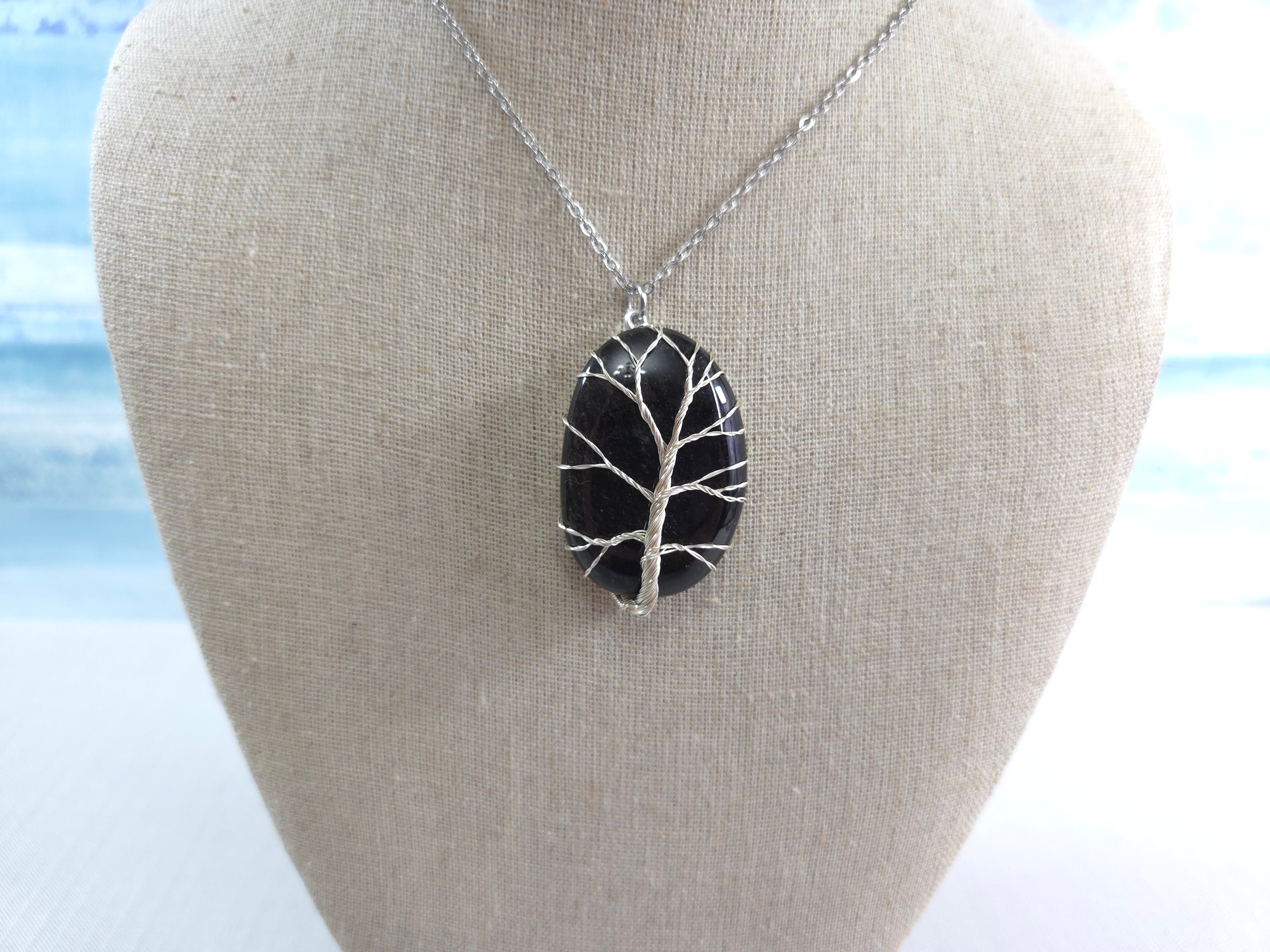 Black tree of life pendant on a silver chain displayed on a bust against a light background