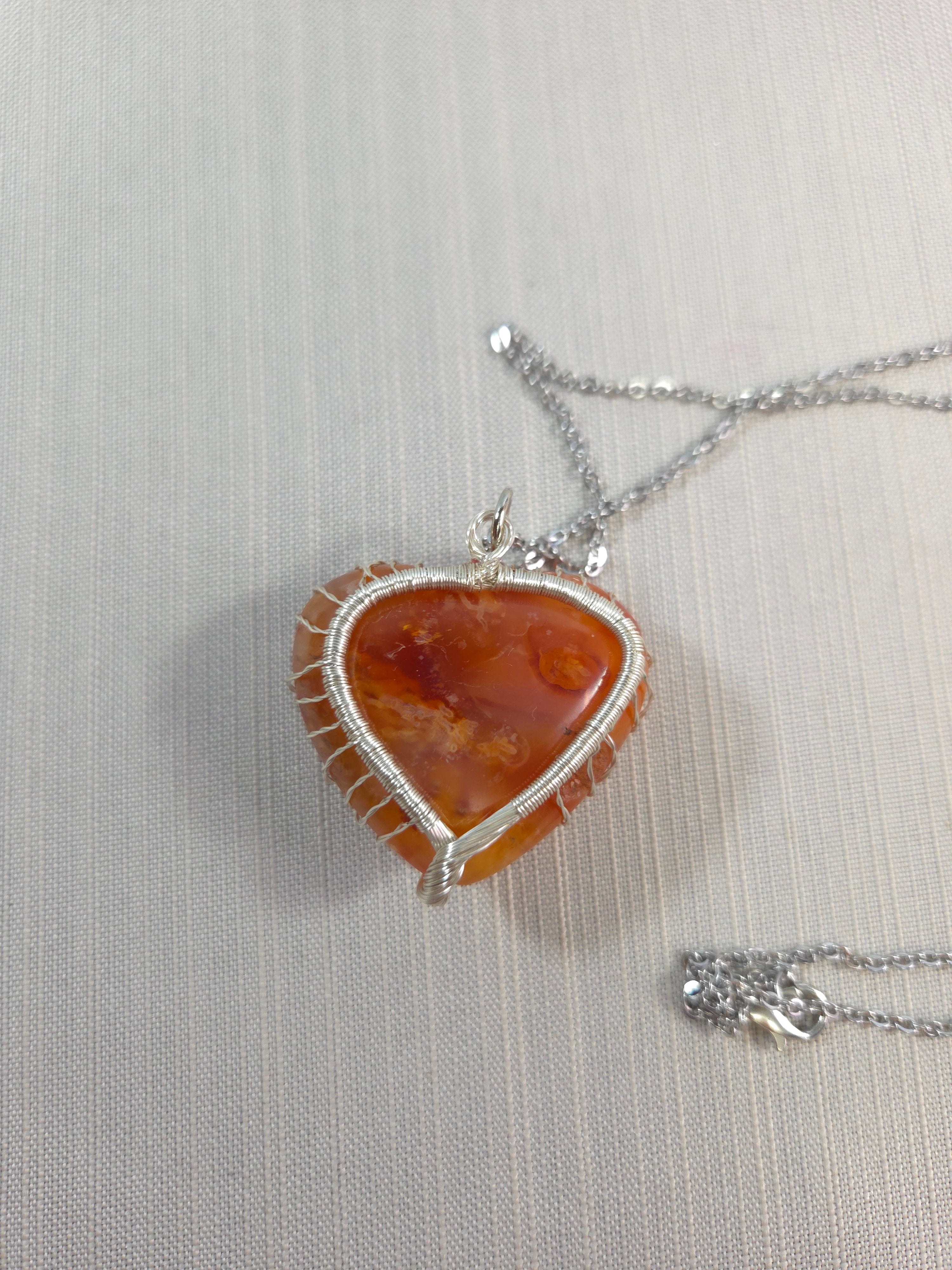 Necklace with a pendant featuring a large orange stone and silver wire wrapping on a light gray background.