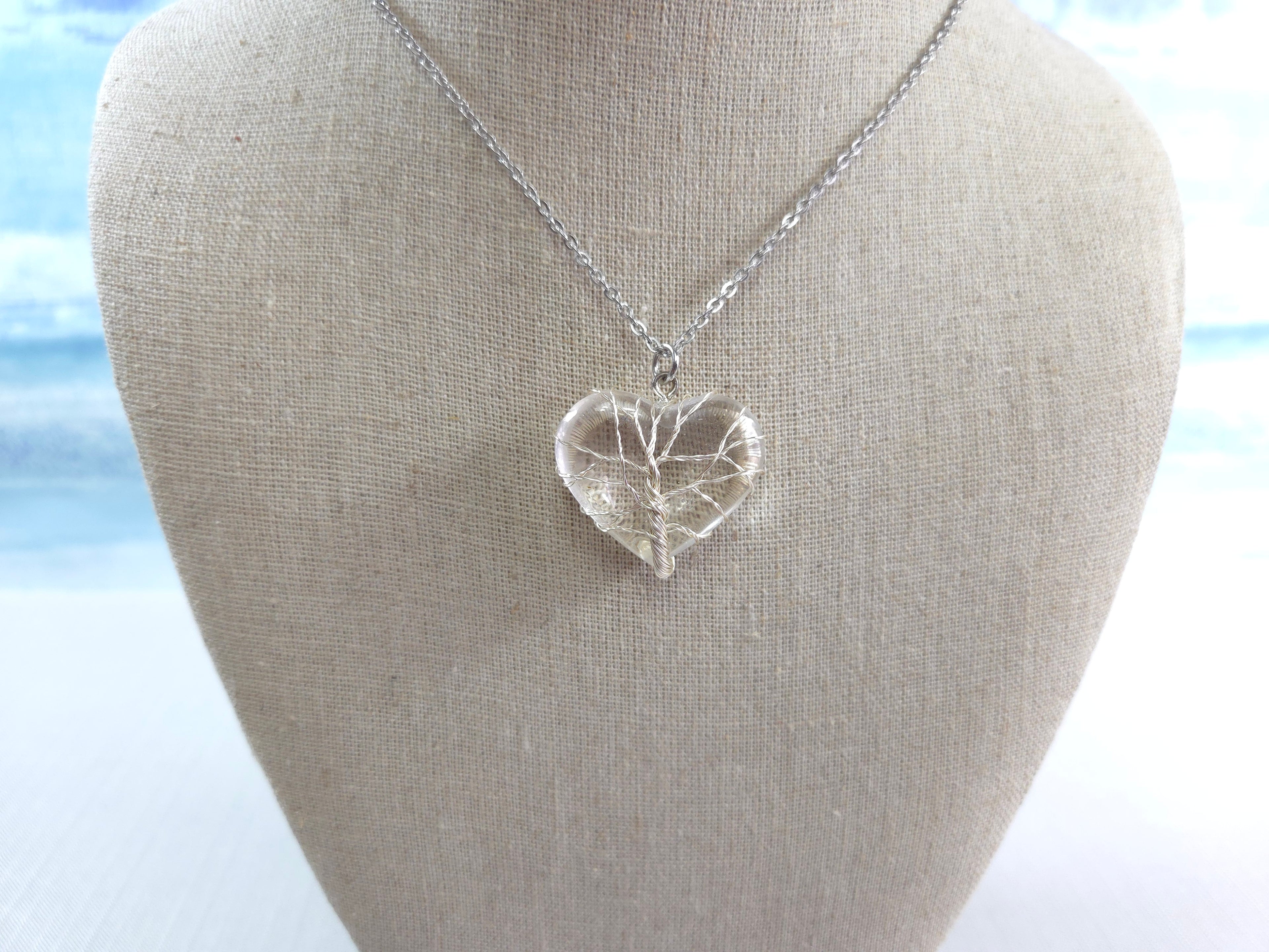 Silver heart-shaped pendant necklace on a mannequin bust with a blurred natural background