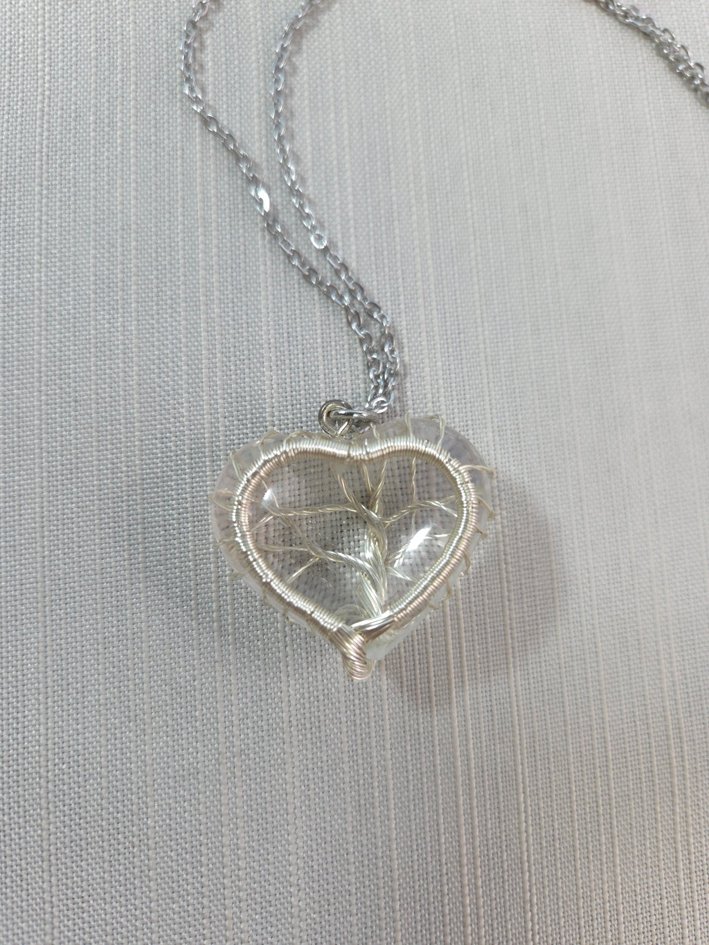Silver heart-shaped pendant on a chain against a light gray background