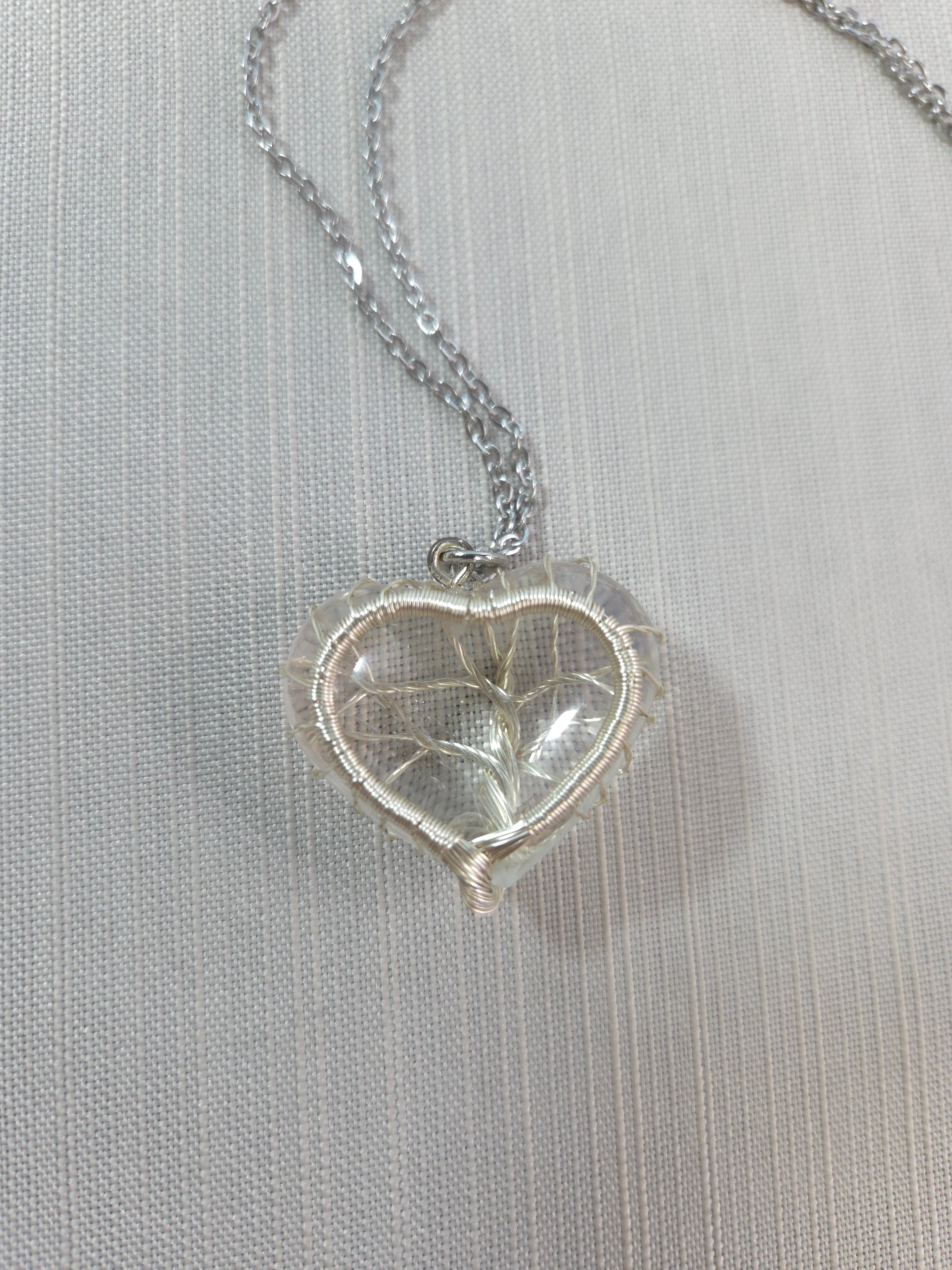 Silver heart-shaped pendant on a chain against a light gray background